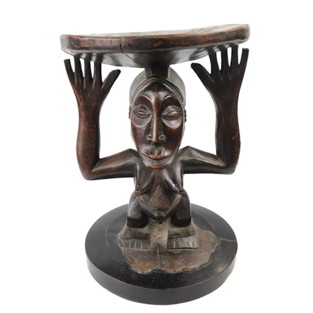 A LUBA CARVED WOODEN STOOL the circular dished top supported...