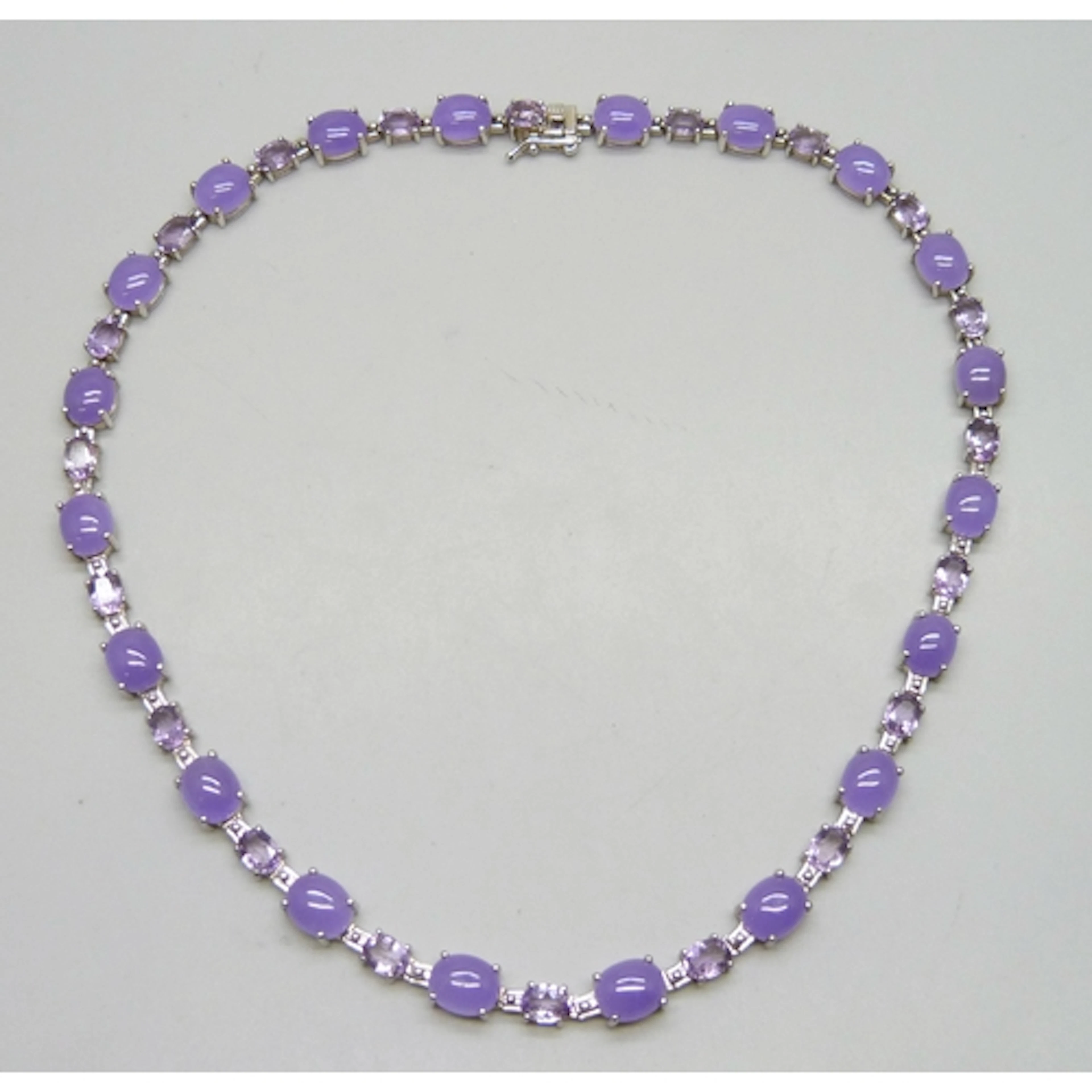 A silver tennis necklace set with amethyst and cabochon purp...