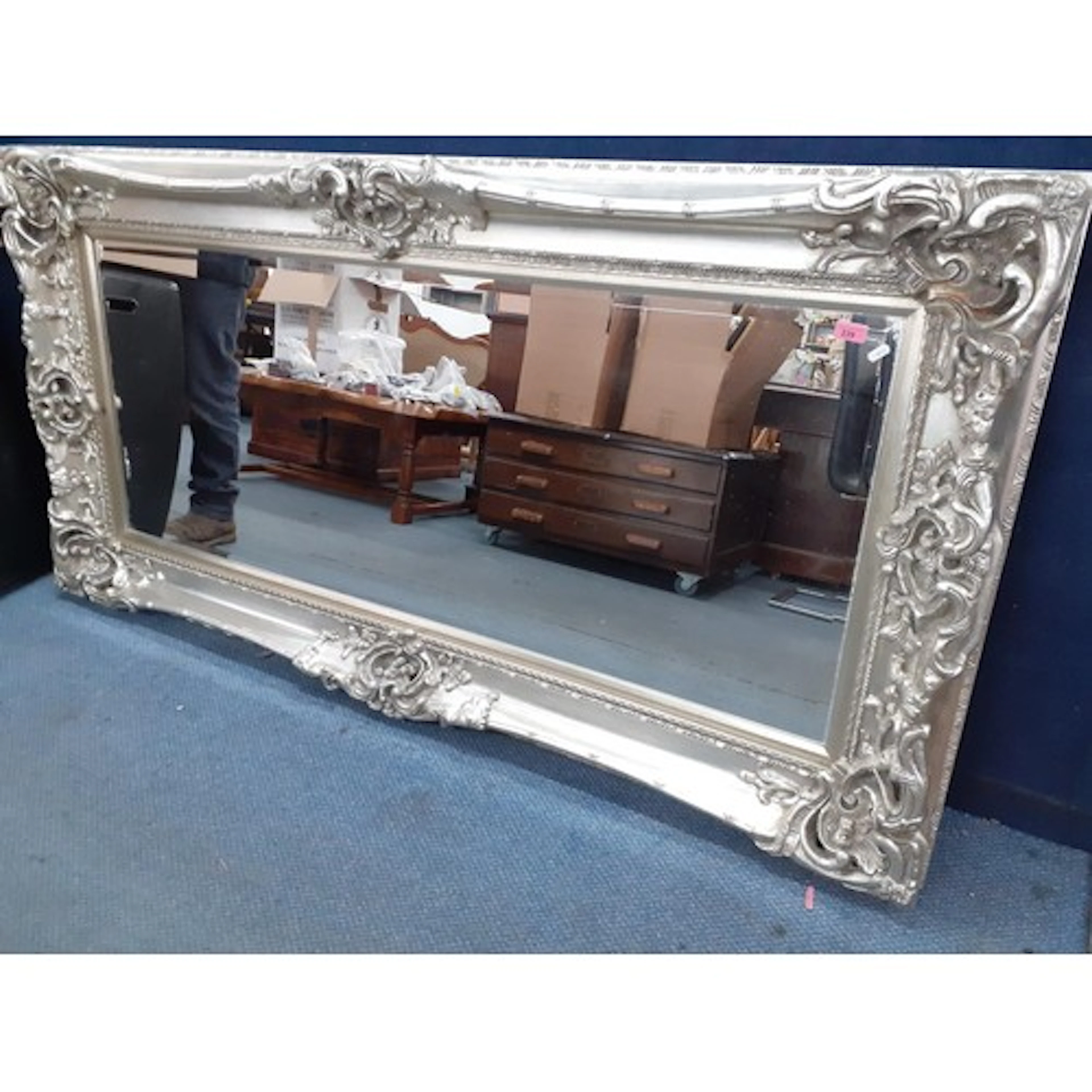 A large modern silver coloured mirror, having an ornate moul...