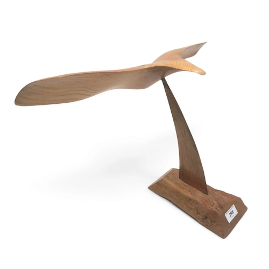 A carved wooden sculpture of a bird suspended on a copper su...