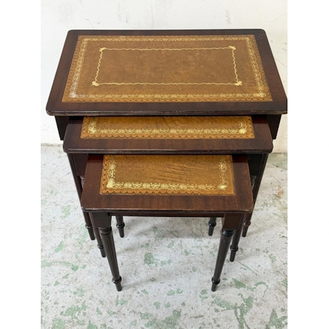 A set of three nesting table with tooled leather top. ...