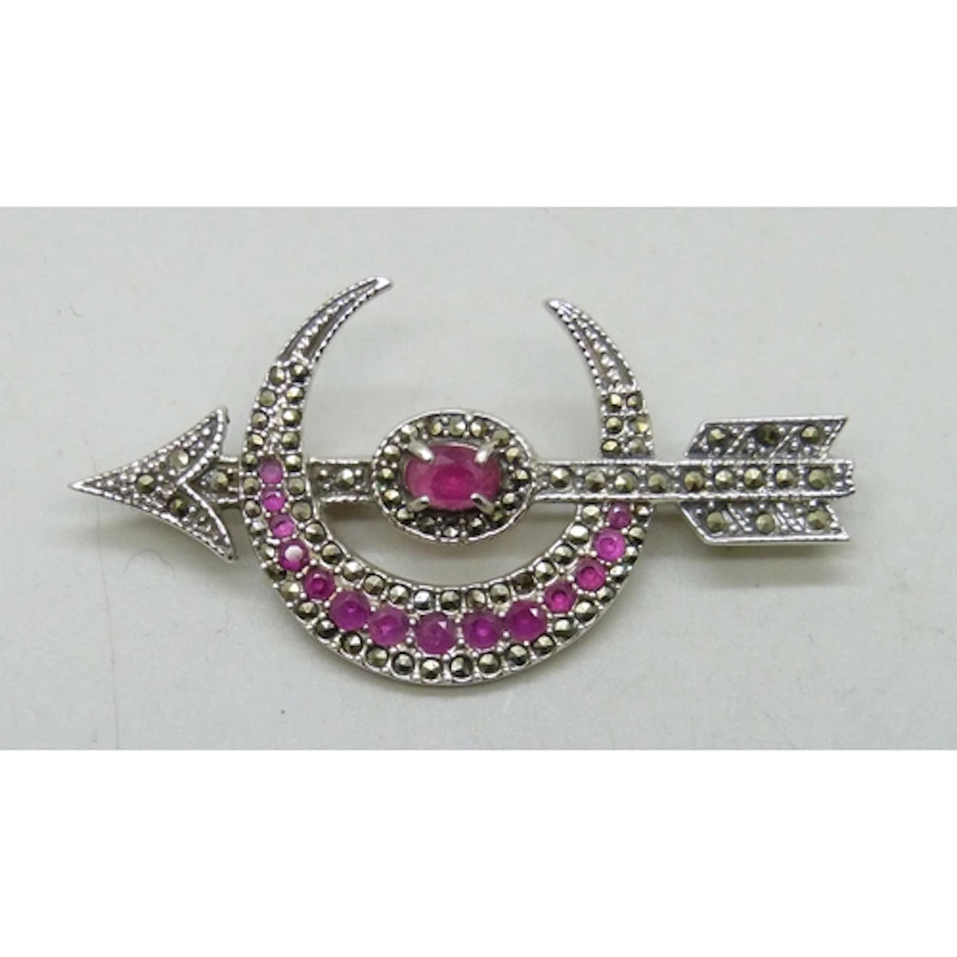 A silver crescent and arrow design brooch set with rubies an...