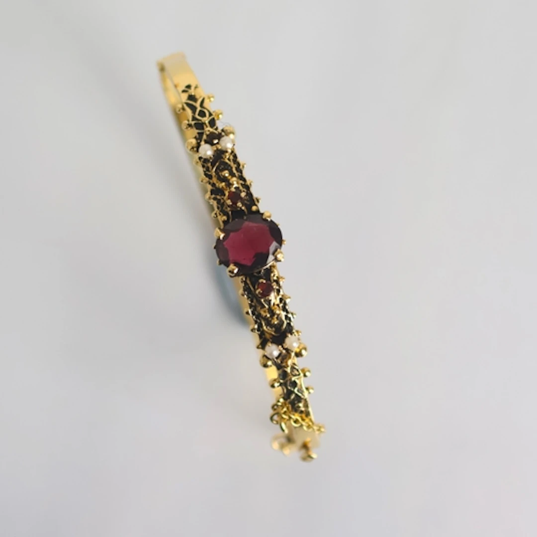 A 19th century style yellow metal garnet bangle, the central...