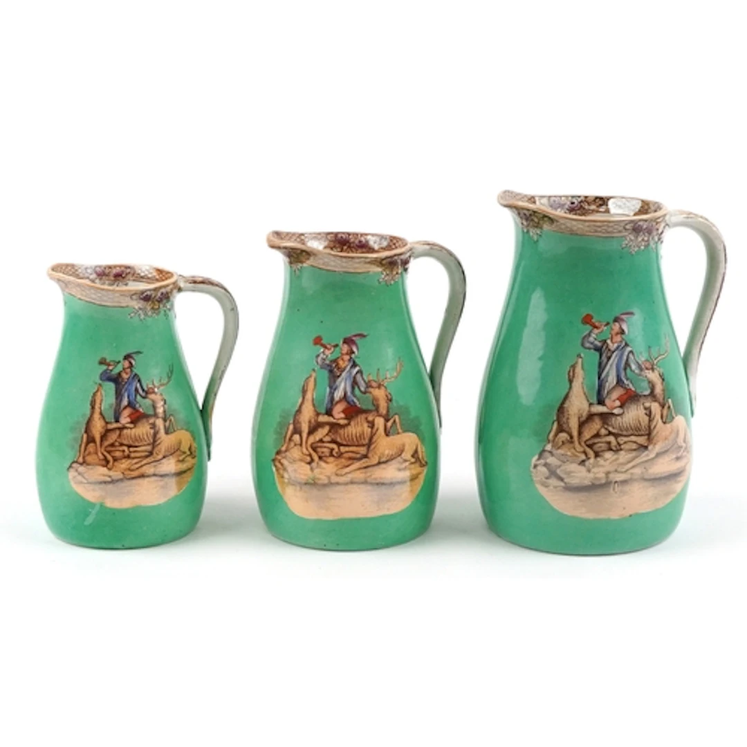 Graduated set of three Victorian pottery jugs on a green gro...