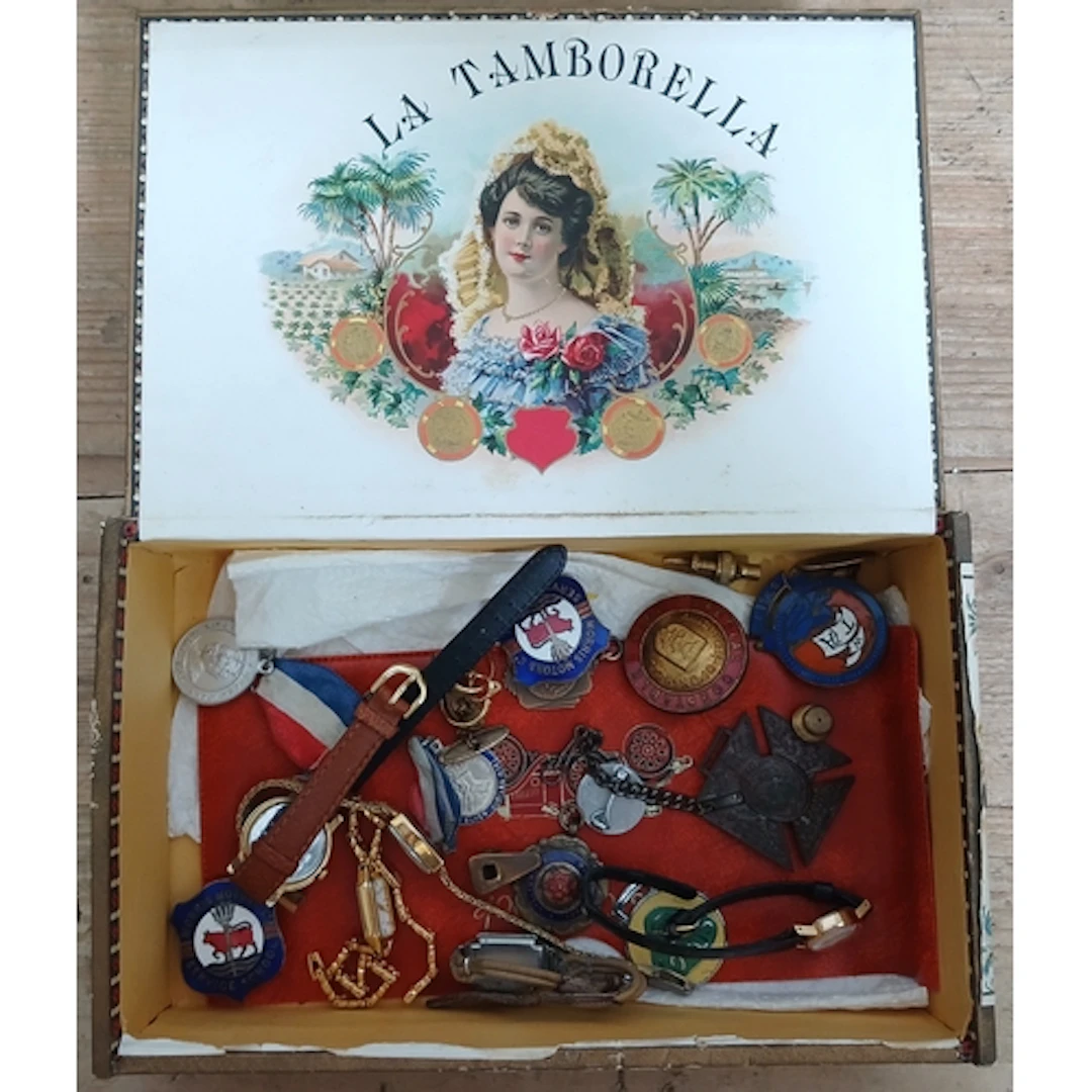 A cigar box of assorted collectables including badges etc.