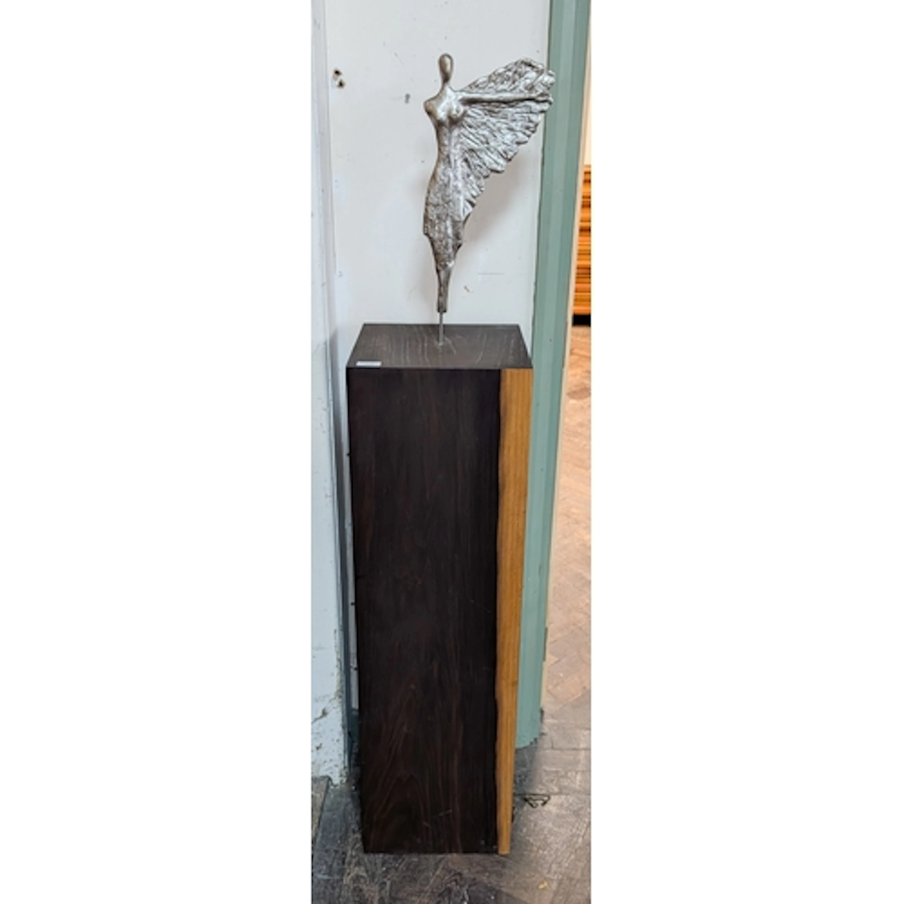 A modern statement sculpture of a winged dancer on a tall wo...