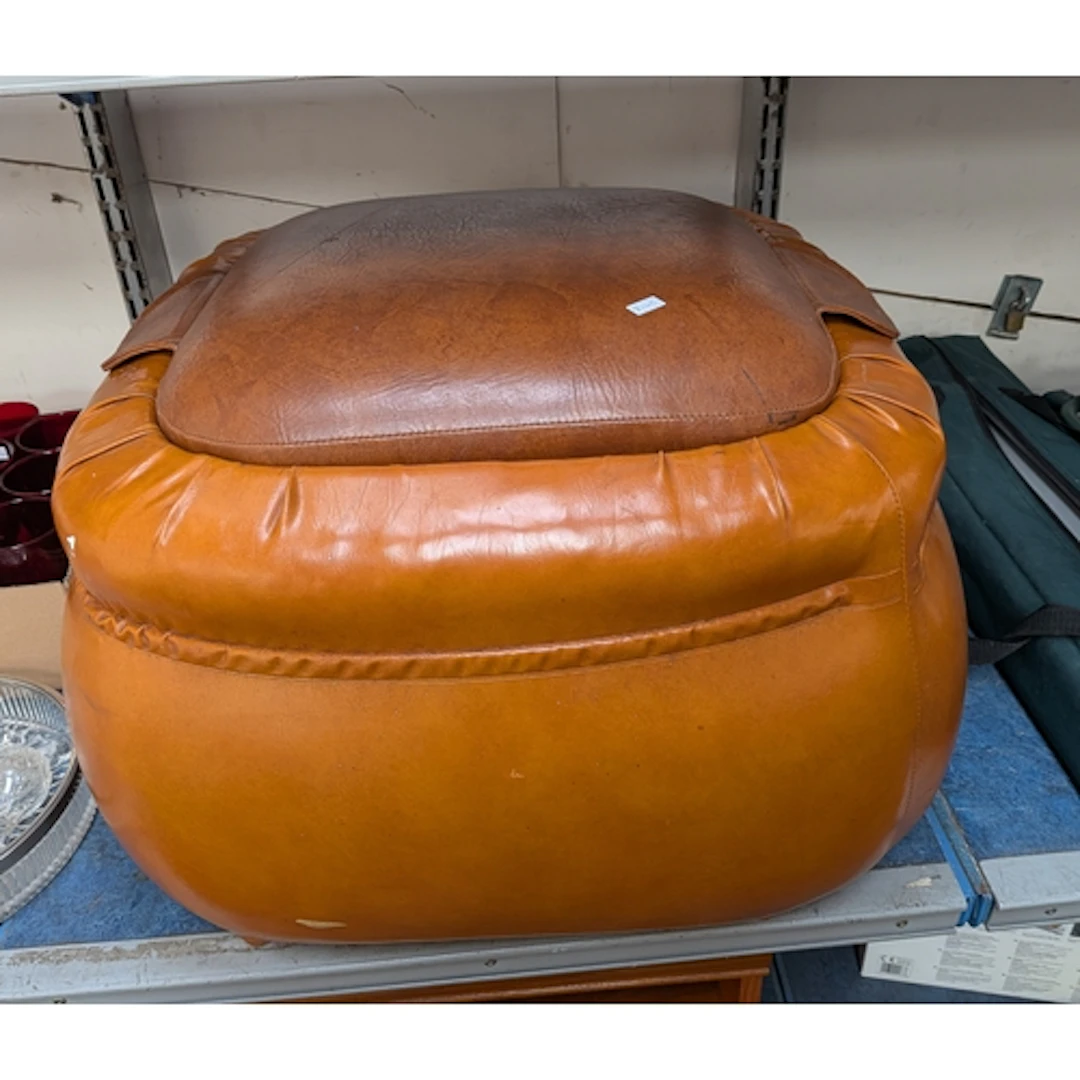 A large brown leather footstool or storage ottoman