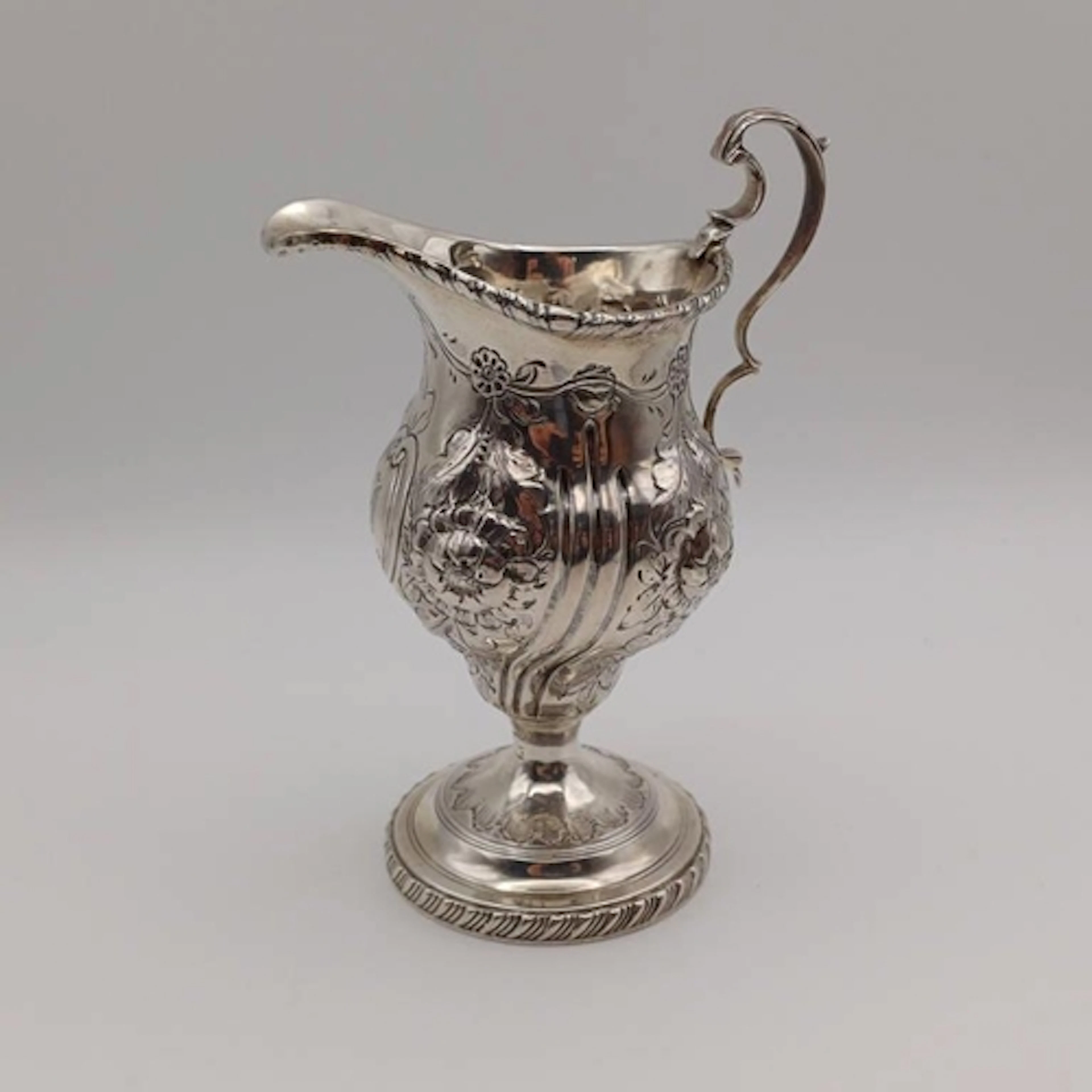 A VICTORIAN SILVER CREAM JUG WITH EMBOSSED FLORAL DECORATION...