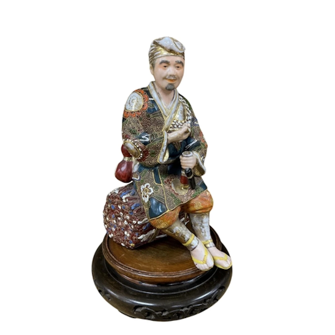 A Japanese Meiji period Satsuma figure of a seated man on as...