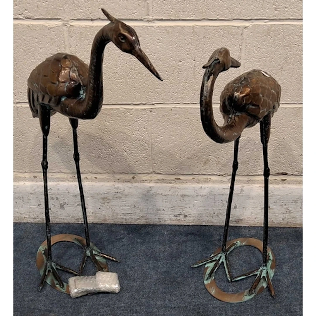 TWO COPPERIZED METAL CRANES, one facing backwards, raised on...