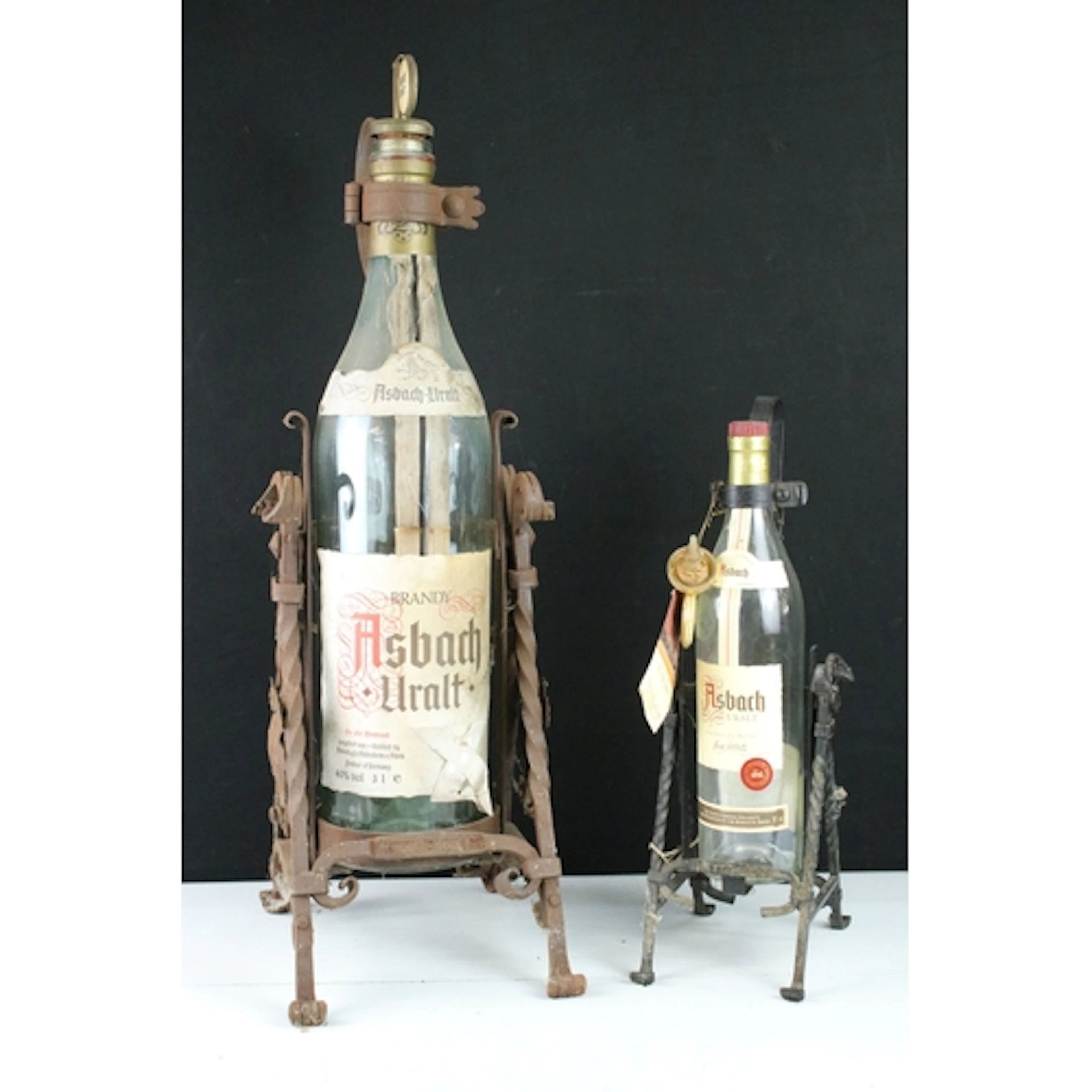 Two wrought iron tilting bottle cradles, one for a 70cl bott...