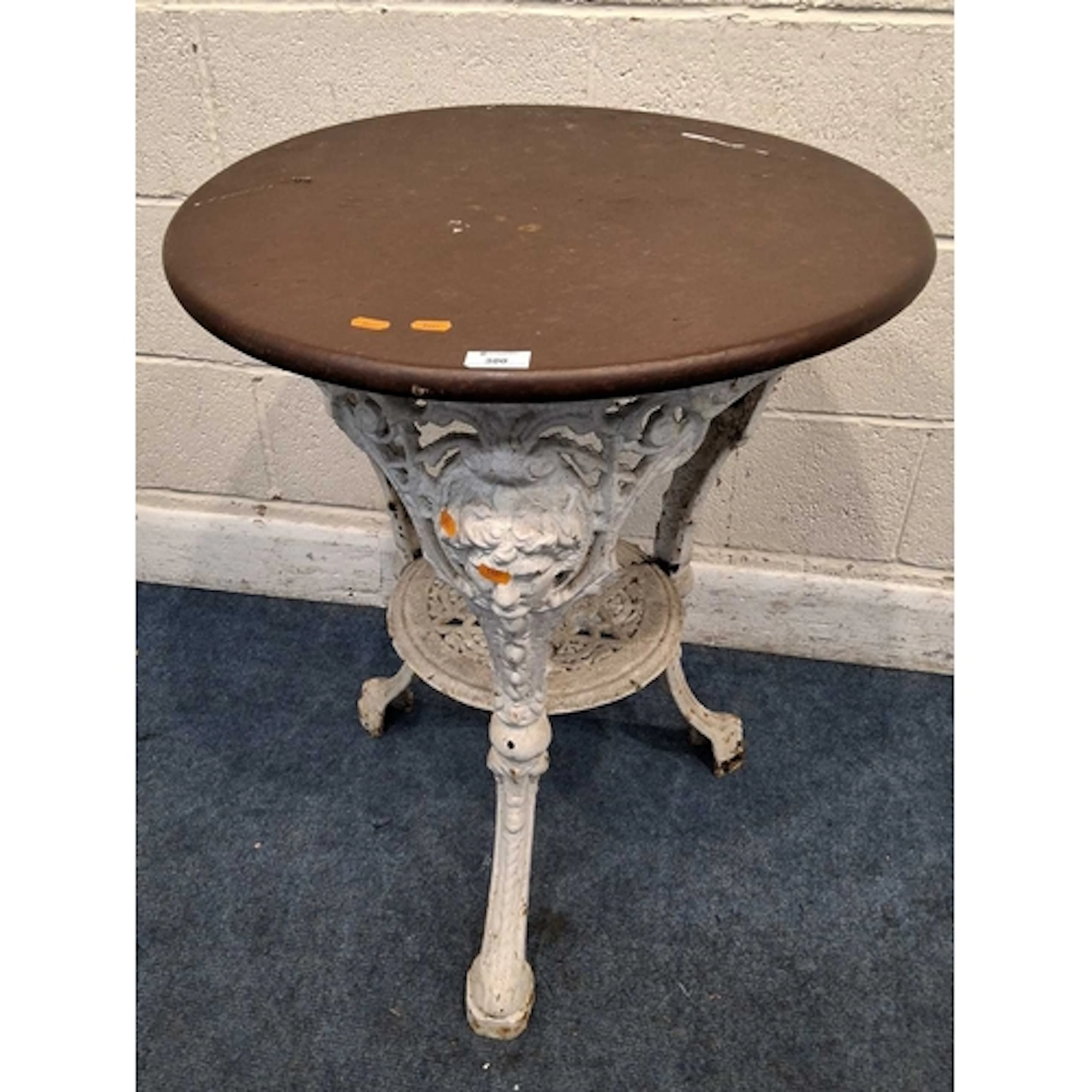 A WHITE PAINTED CAST IRON PUB TABLE, with masks on each leg,...