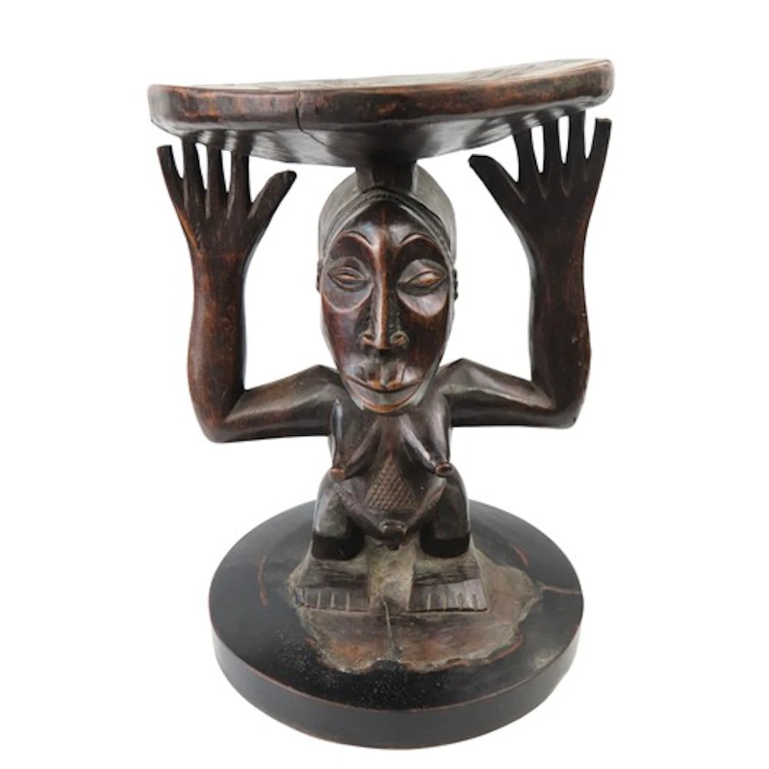 A LUBA CARVED WOODEN STOOL the circular dished top supported...