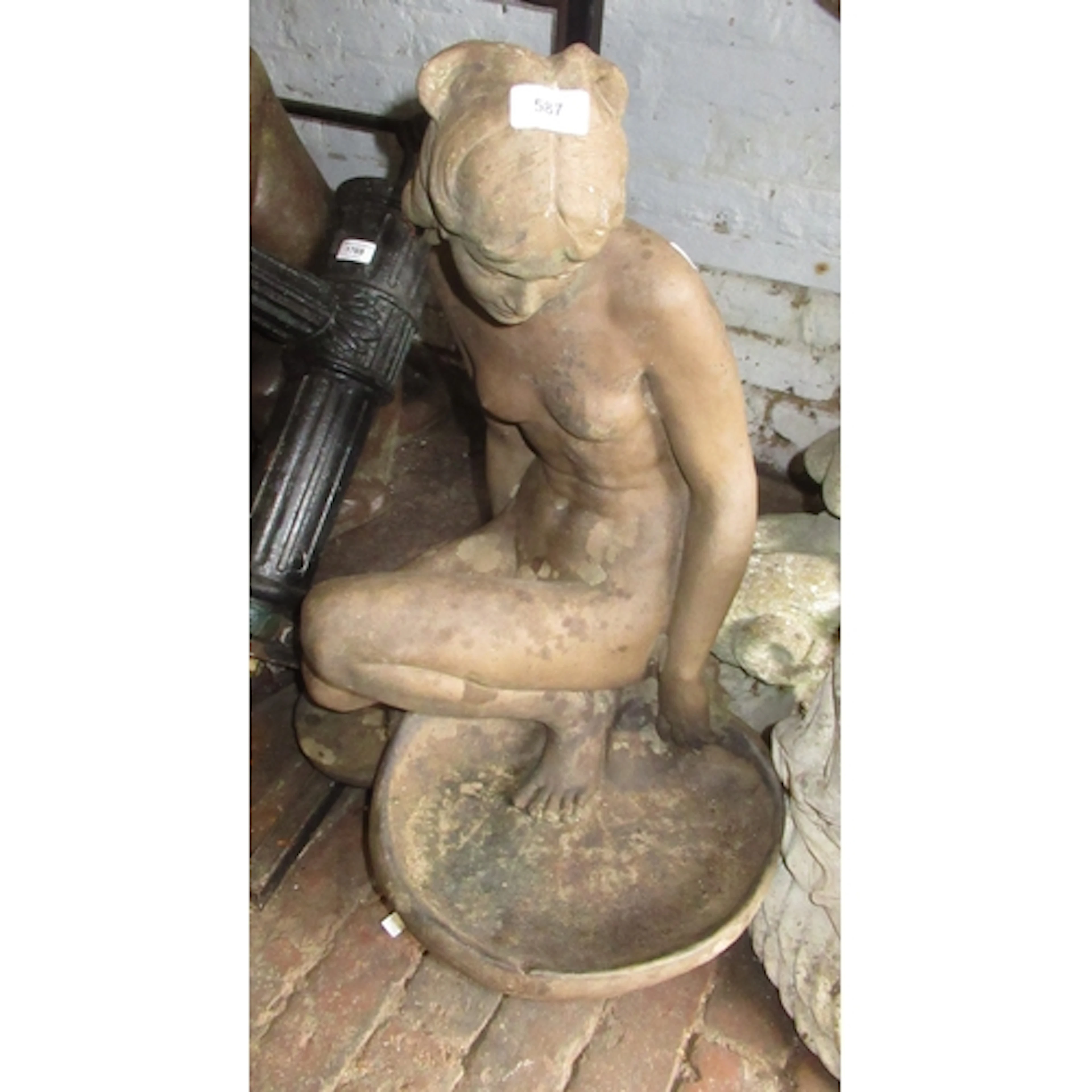 Weathered terracotta garden statue of a kneeling nude female...