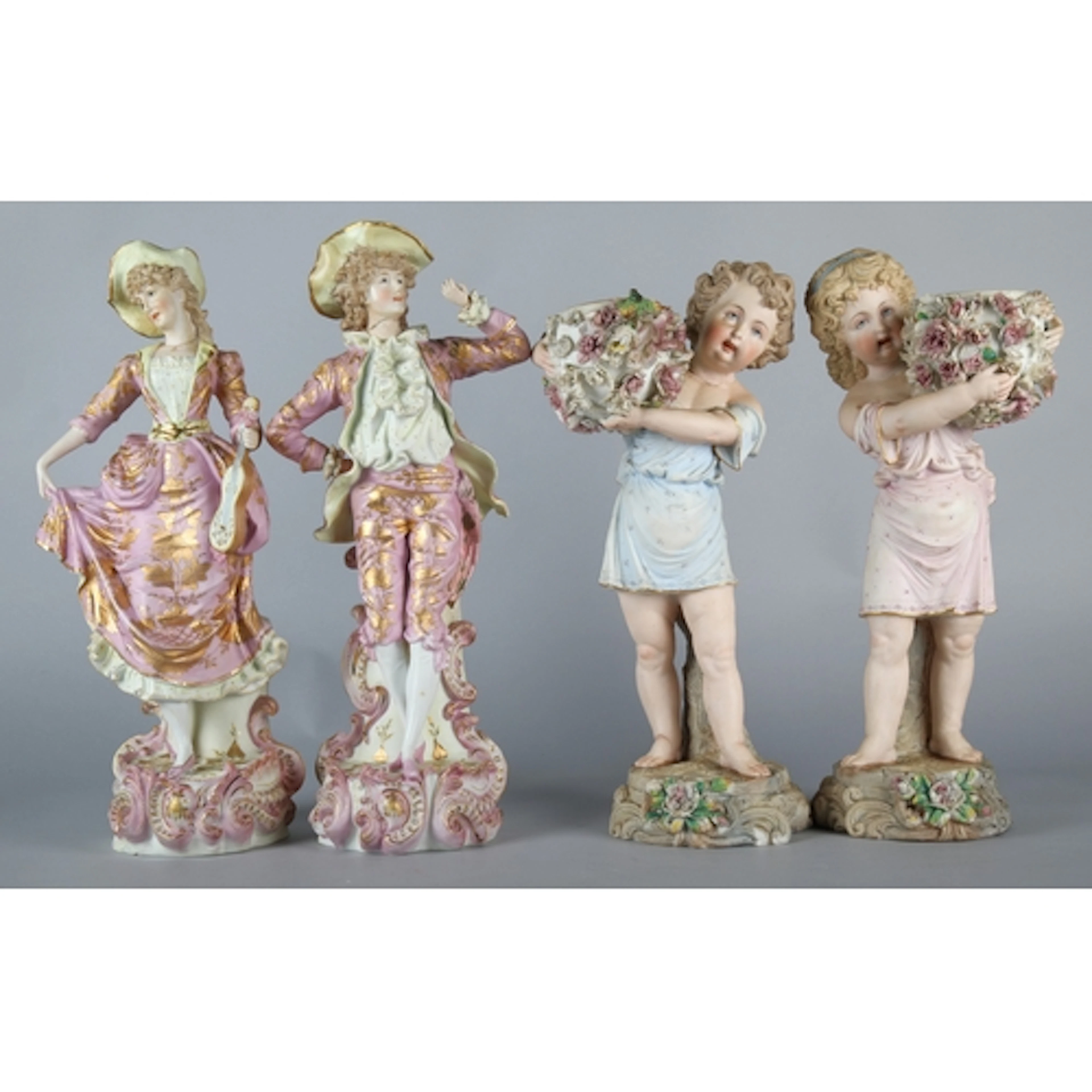 Four bisque figurines, to include two youths holding floral ...