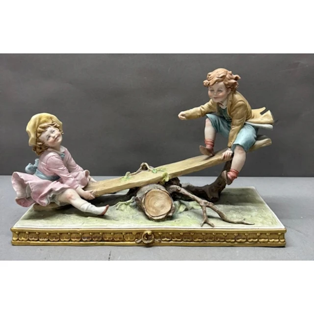 A Capodimonte figural scene of children on a seesaw.