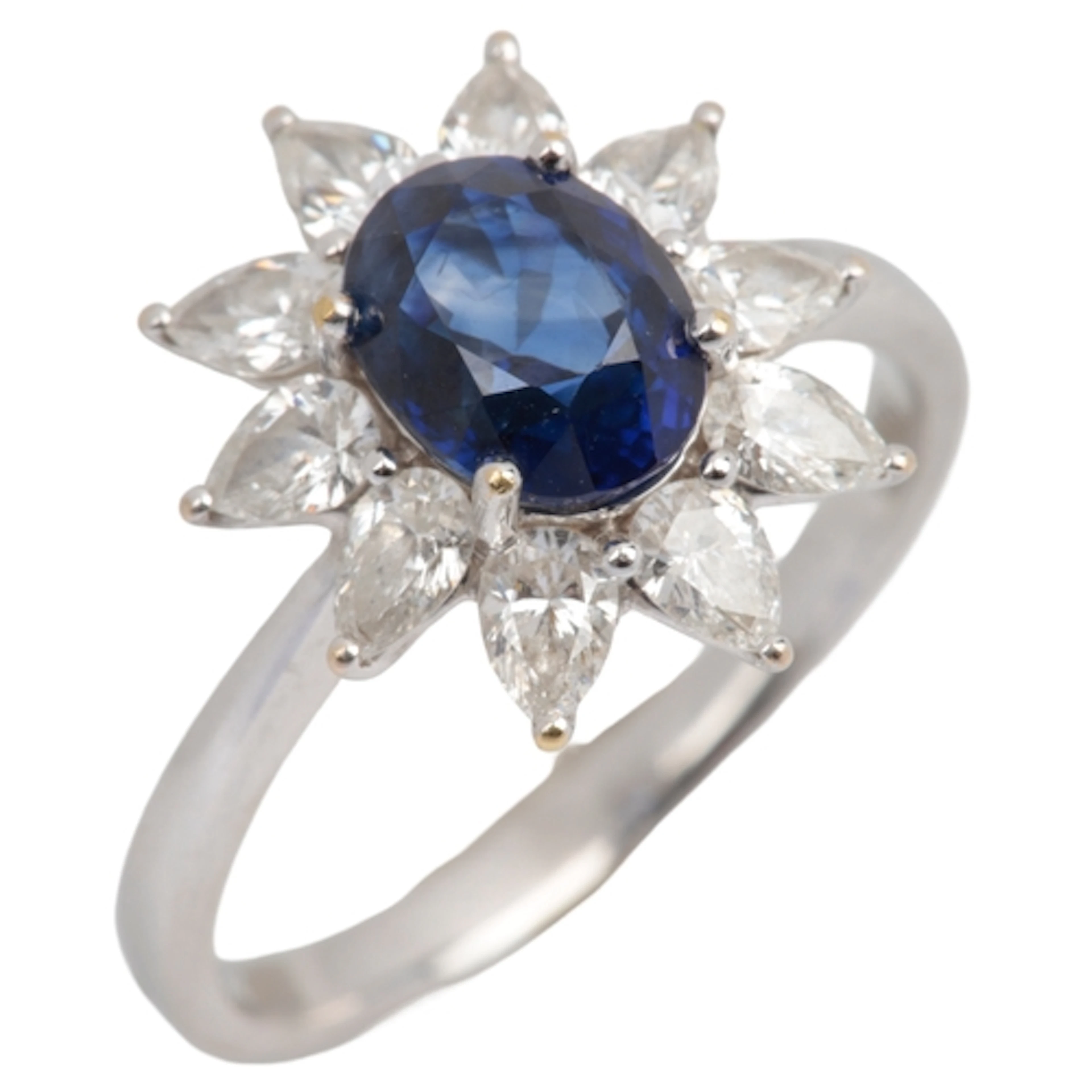 A sapphire and diamond cluster ring, claw-set with an oval s...