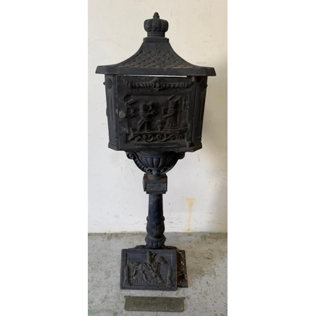 A black cast iron freestanding post box with a pastoral rele...
