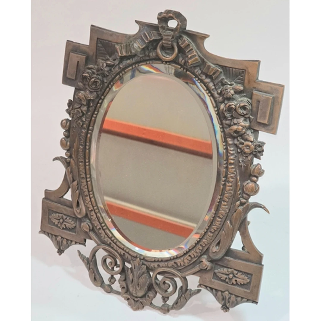 An antique bronze tabletop easel mirror featuring an oval be...