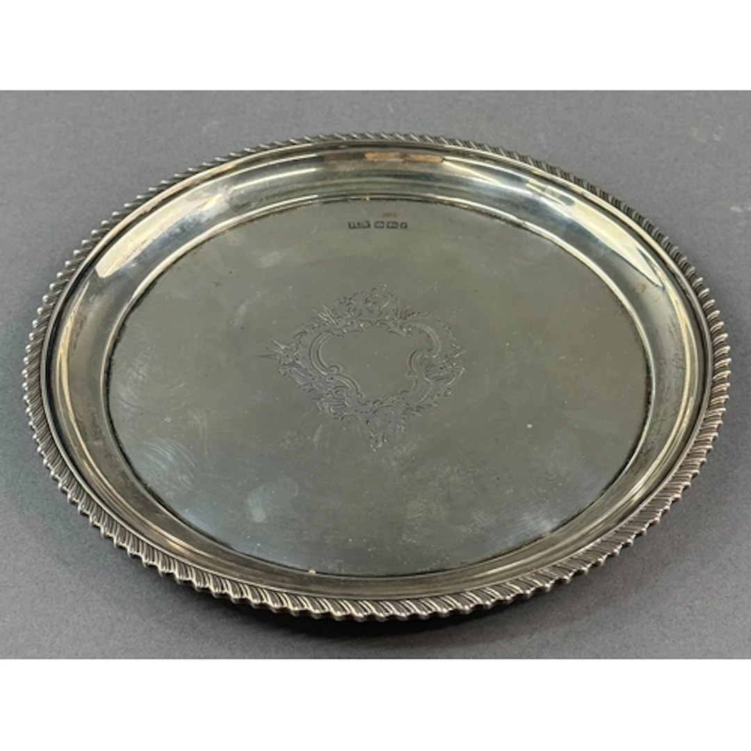 Silver: a circular salver with gadrooned rim and central eng...
