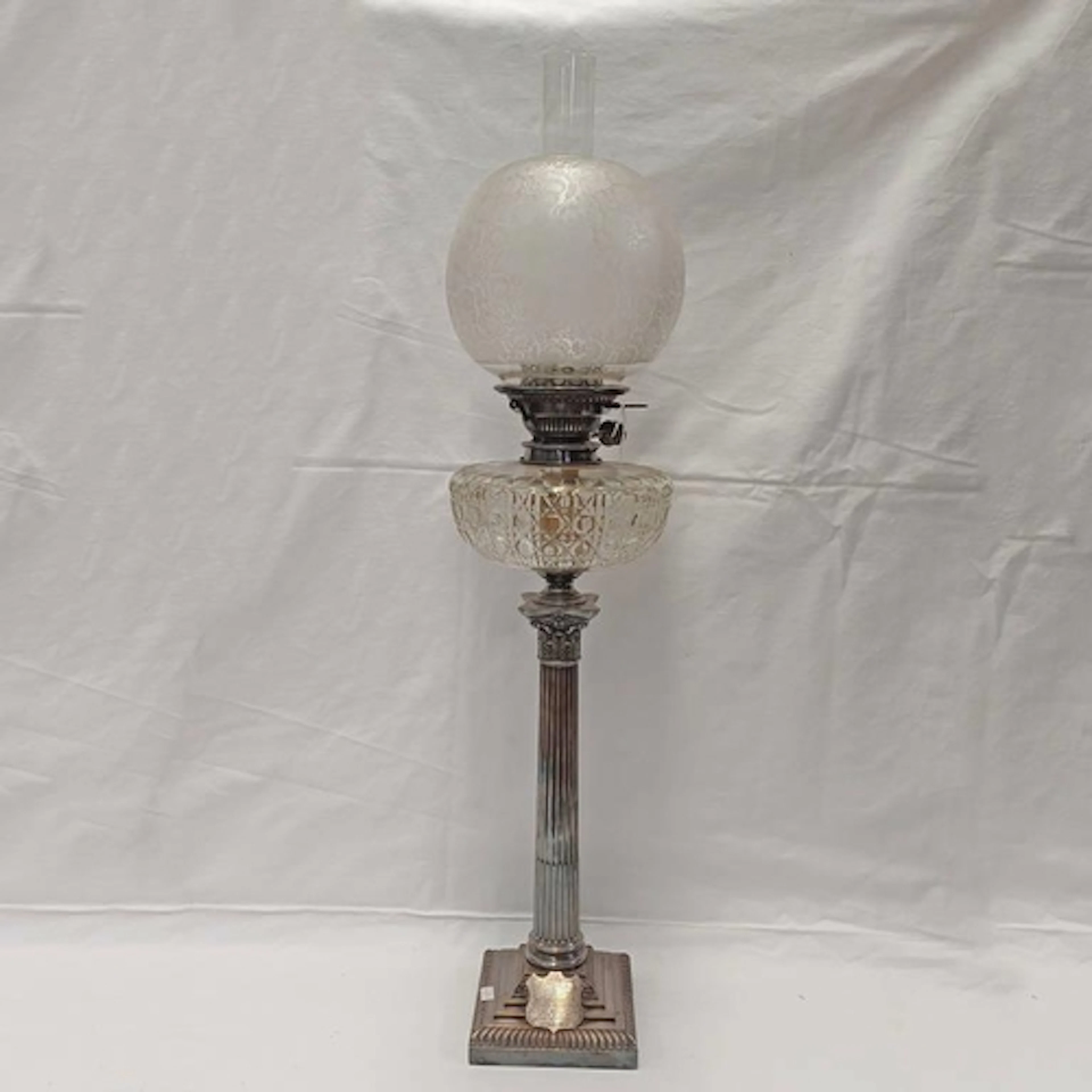 A SILVER PLATED CORINTHIAN COLUMN PARAFFIN LAMP WITH CUT GLA...
