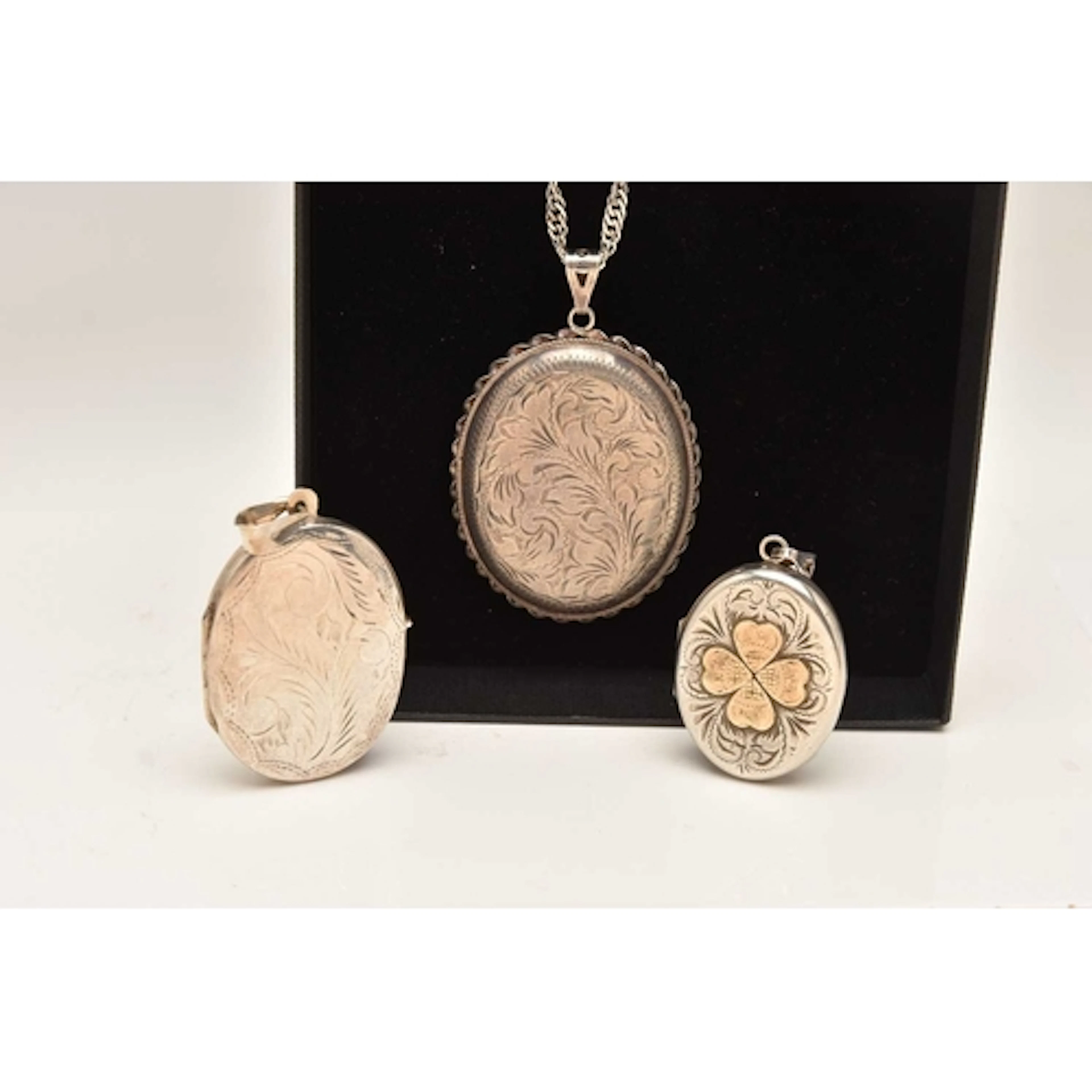 THREE SILVER OVAL PENDANT LOCKETS AND A CHAIN, the larger lo...