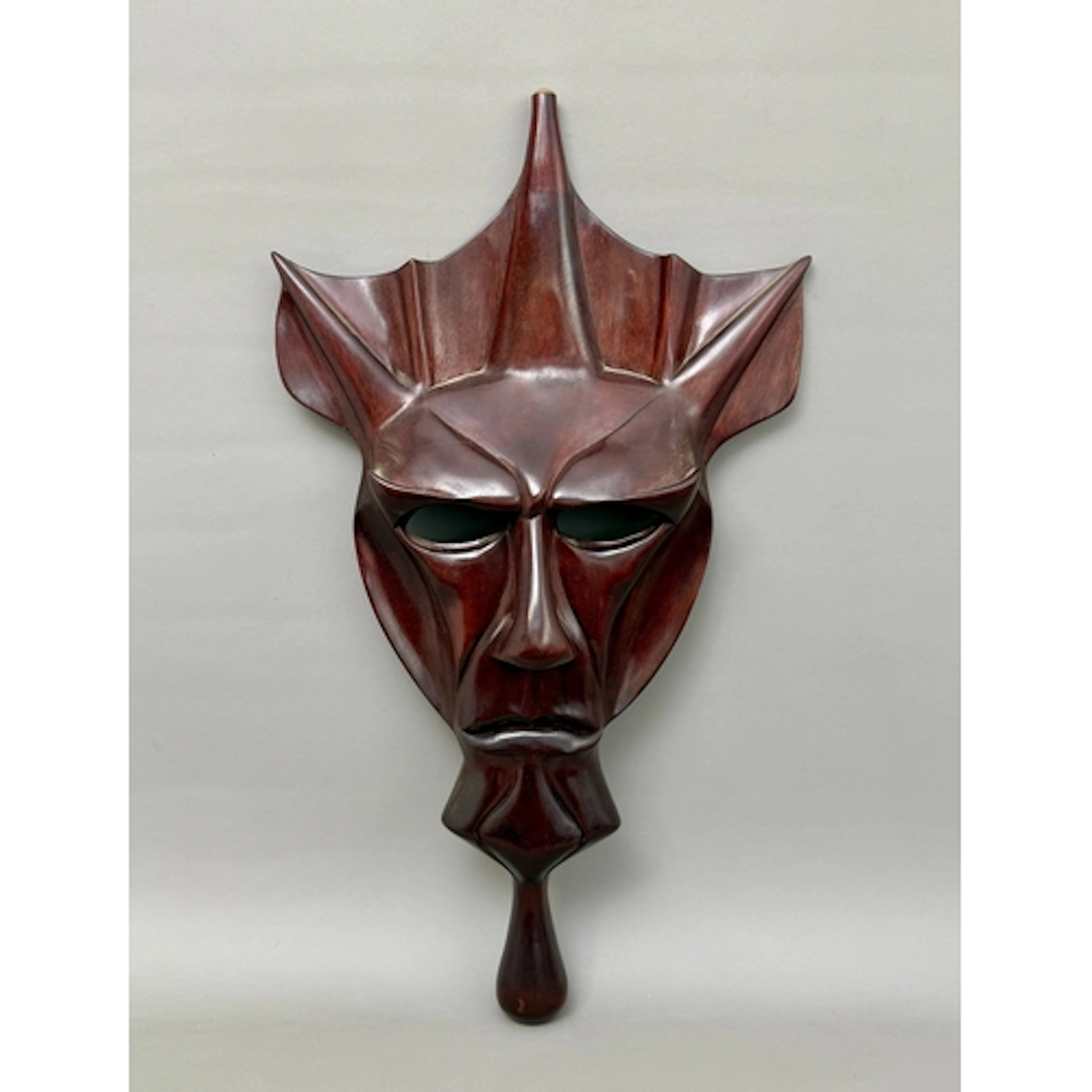 A wooden hand held face mask - of a demon like subject, carv...