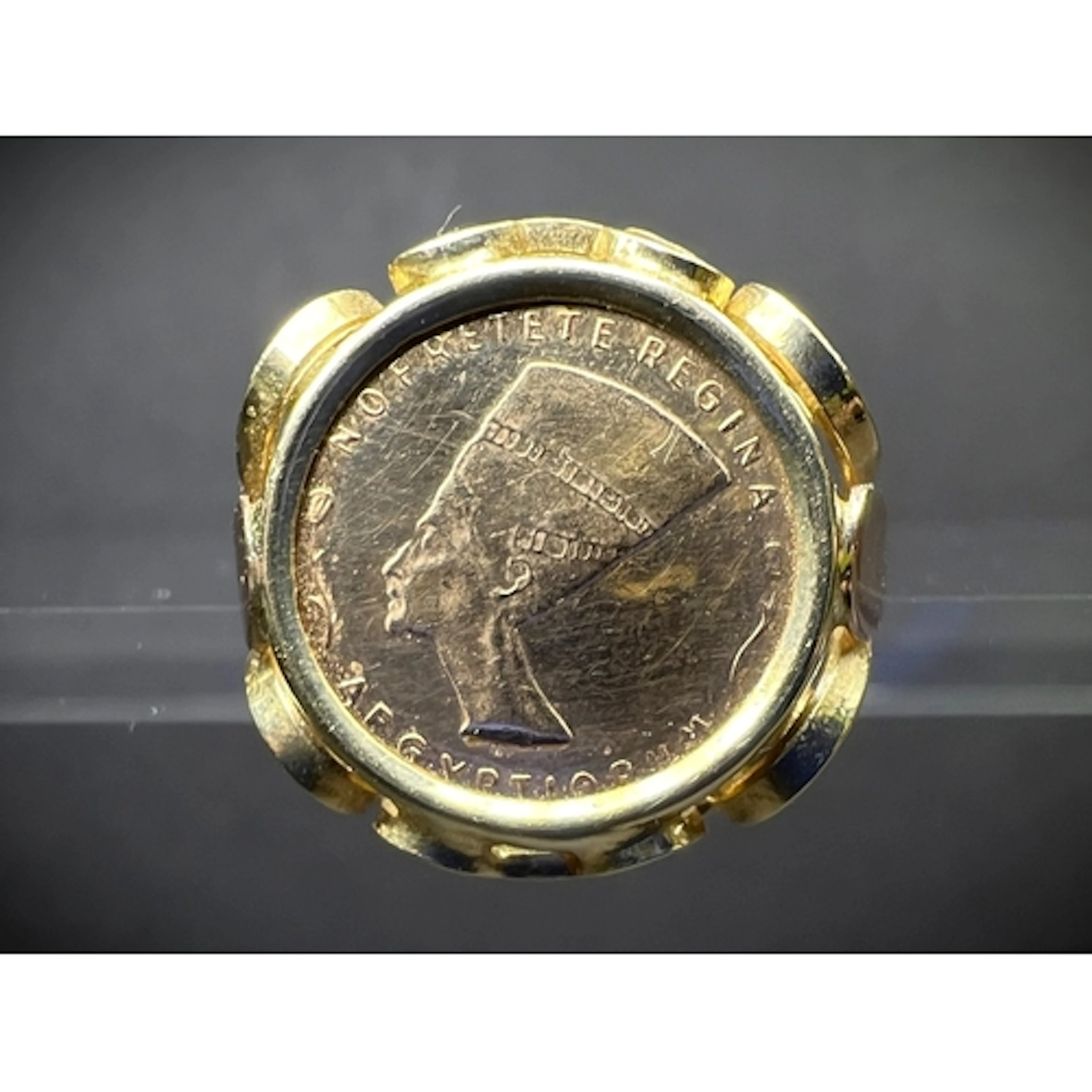 A yellow metal ring set with a coin commemorating Queen Nefe...
