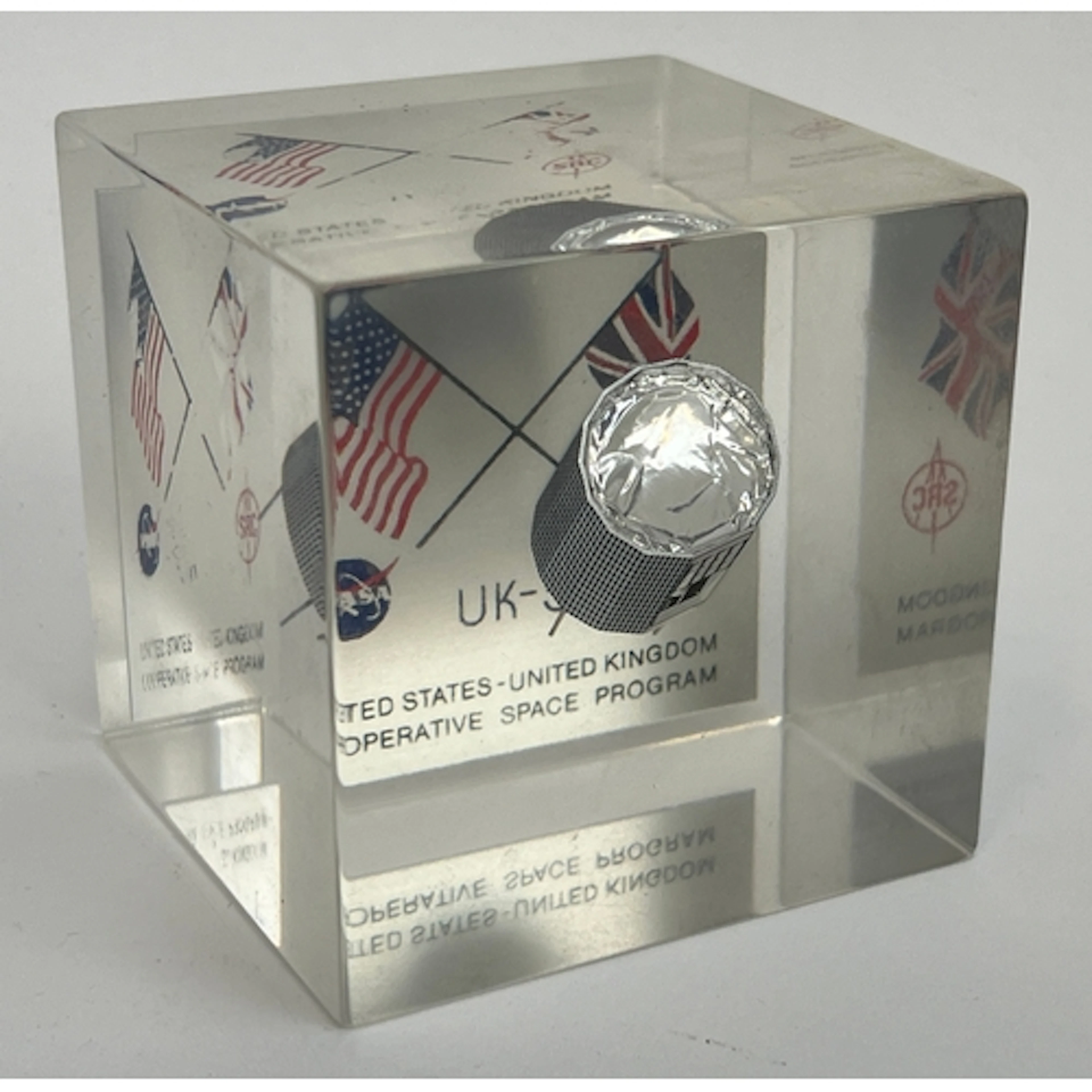 A vintage perspex paperweight commemorating the UK-5 NASA Un...
