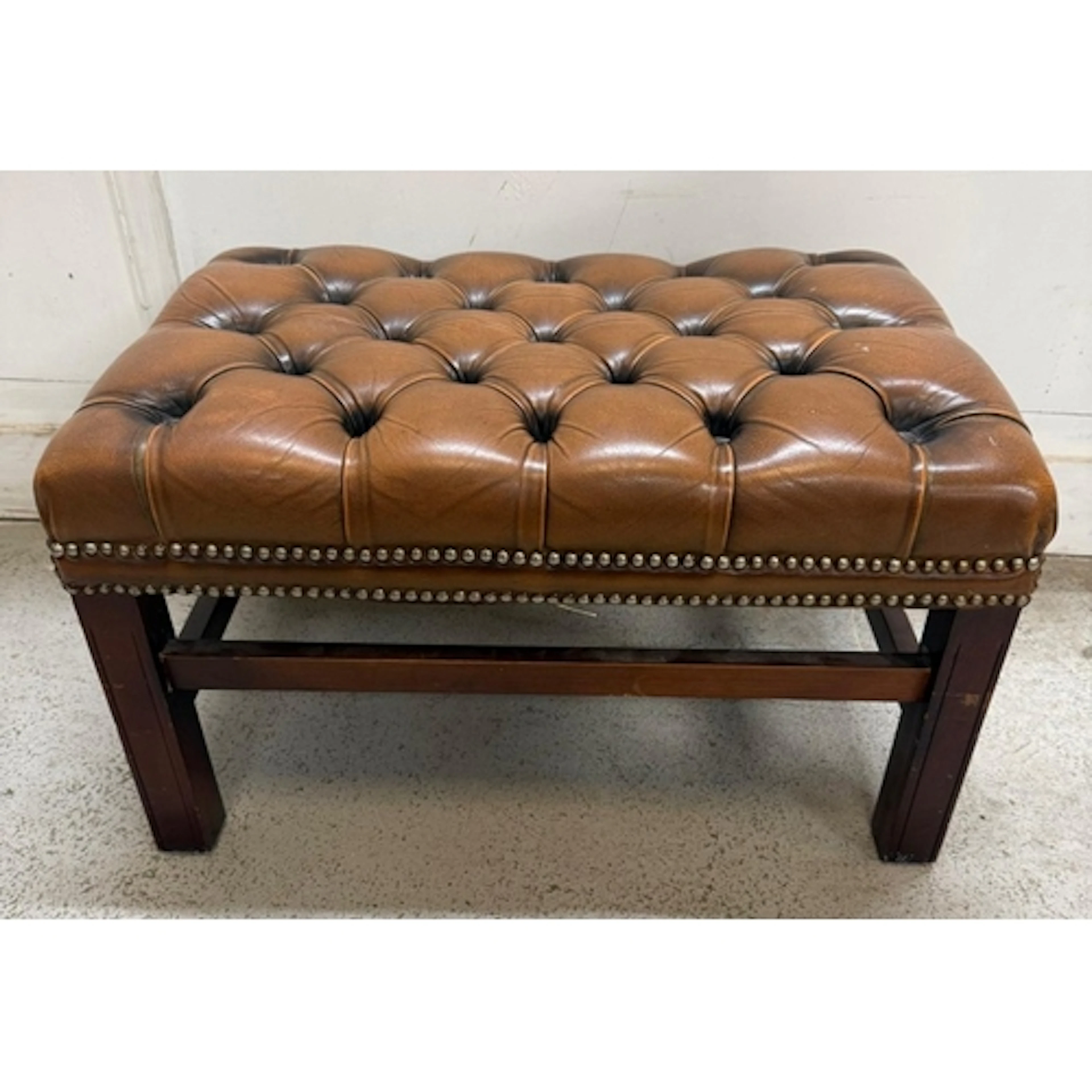 A brown leather button tufted footstool with brass stud deta...