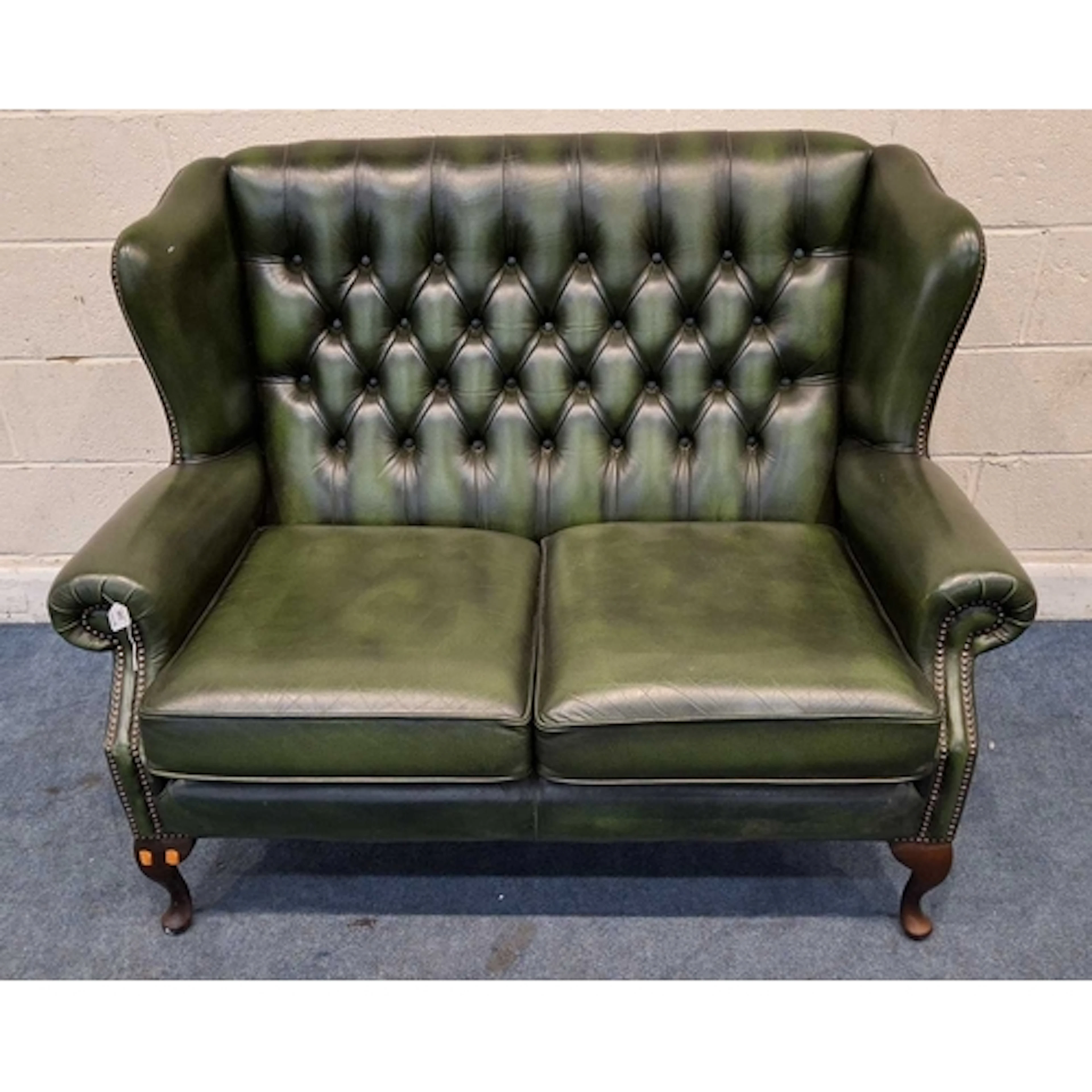 A GREEN LEATHER TWO SEATER WINGBACK SOFA, with buttoned upho...