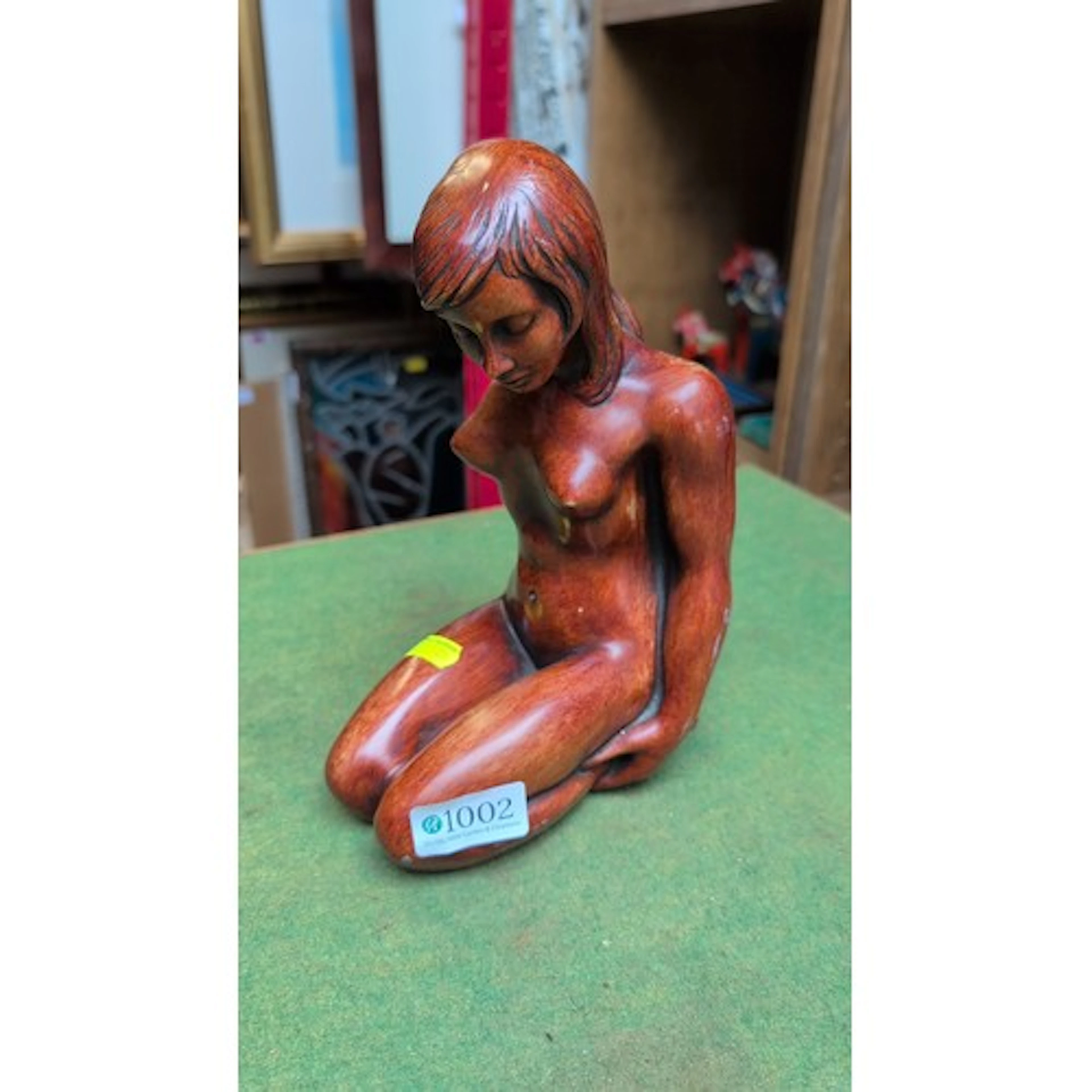 Carved hardwood figure of a kneeling nude female, head bowed...