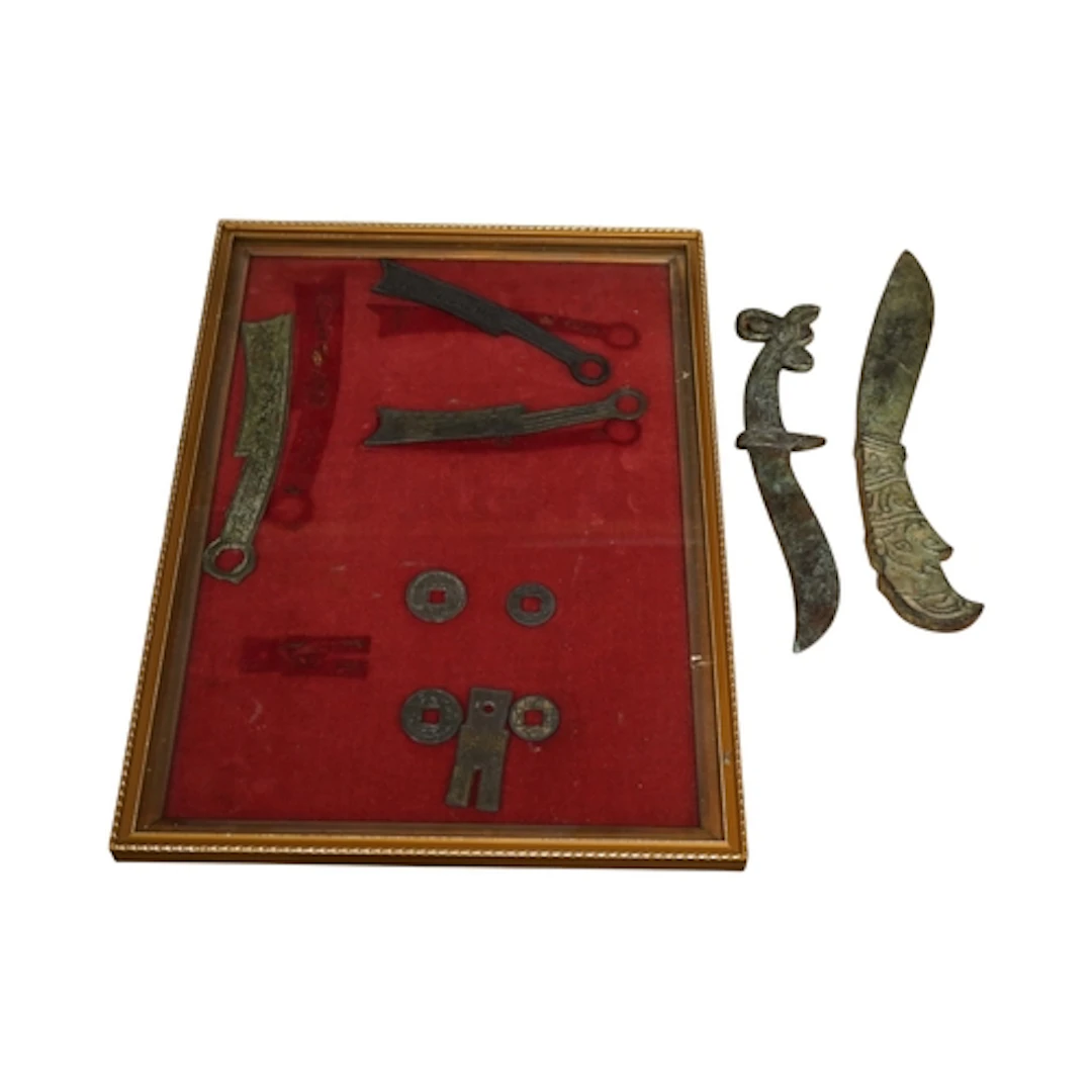 A framed display of Chinese money and two knives