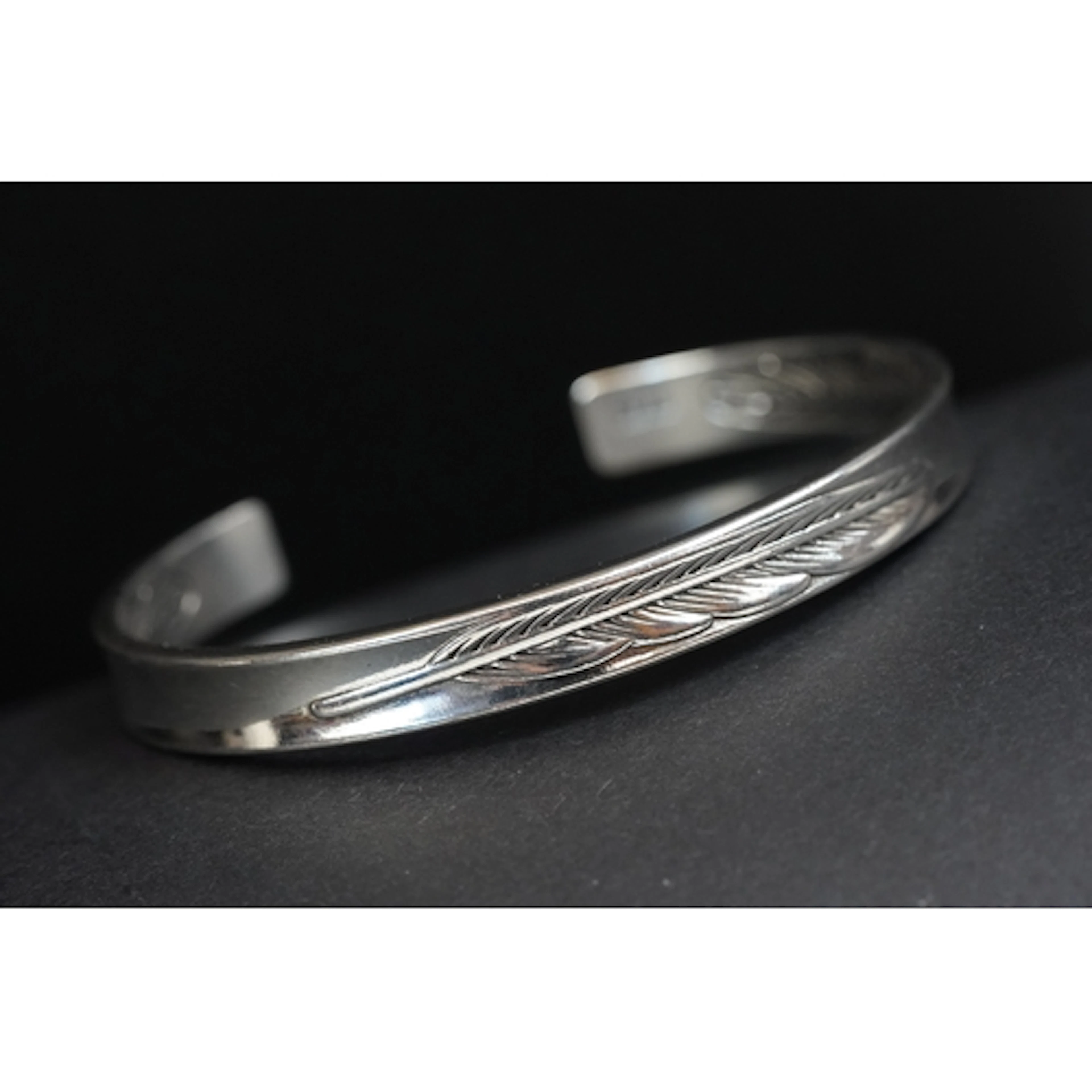 A contemporary silver open backed bangle, feather decoration...