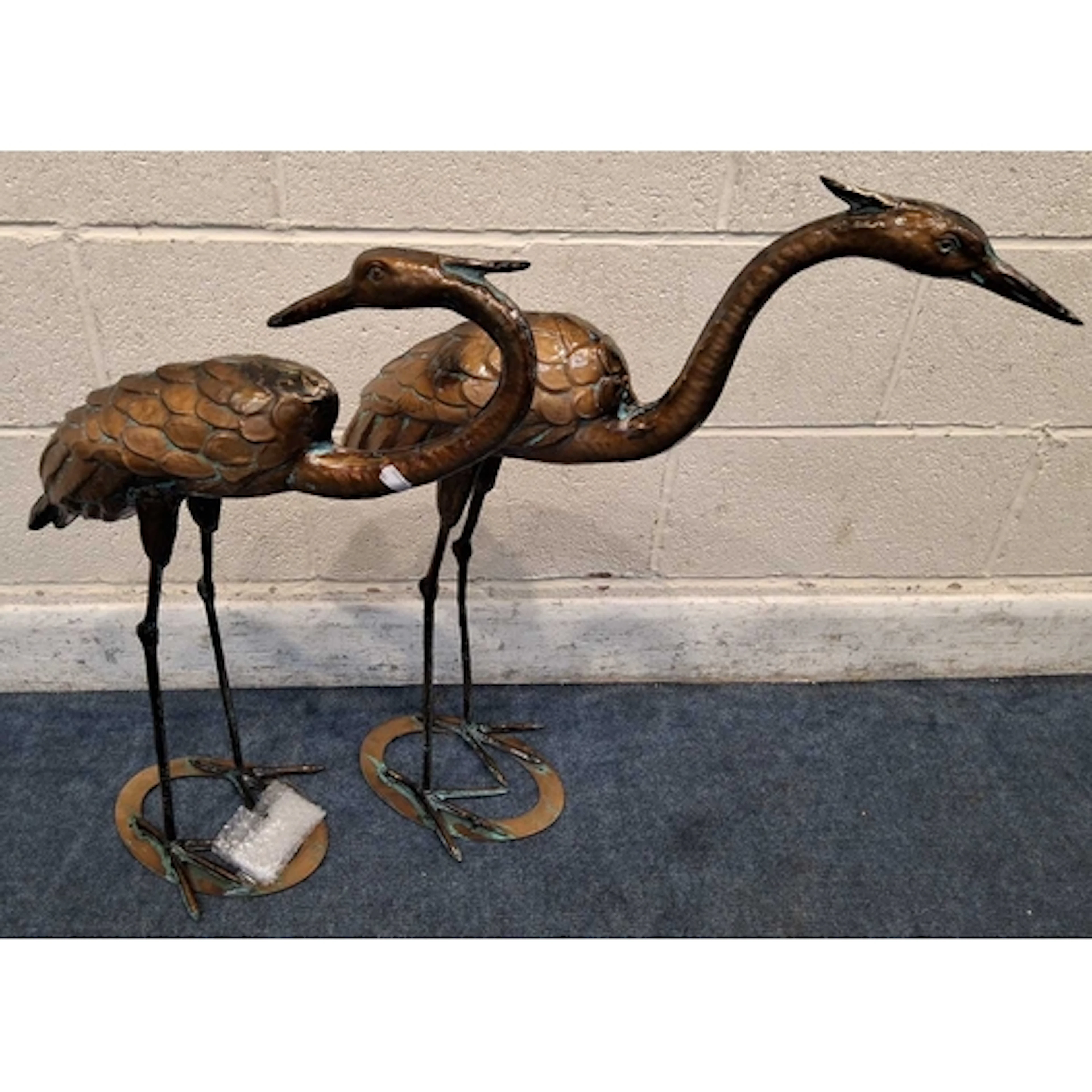 TWO COPPERIZED METAL CRANES, one facing backwards, raised on...