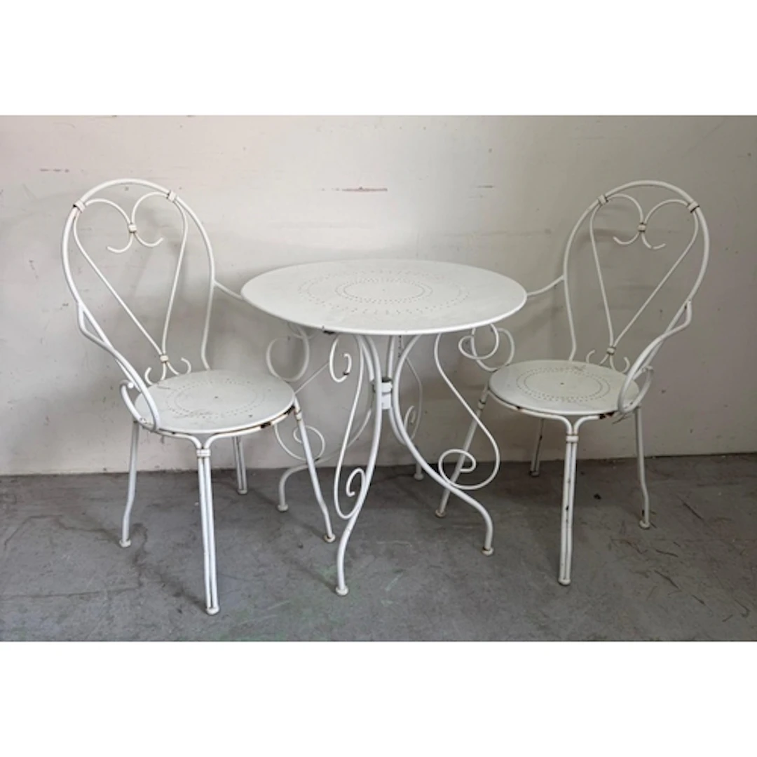 A white metal circular bistro table and two chairs with scro...