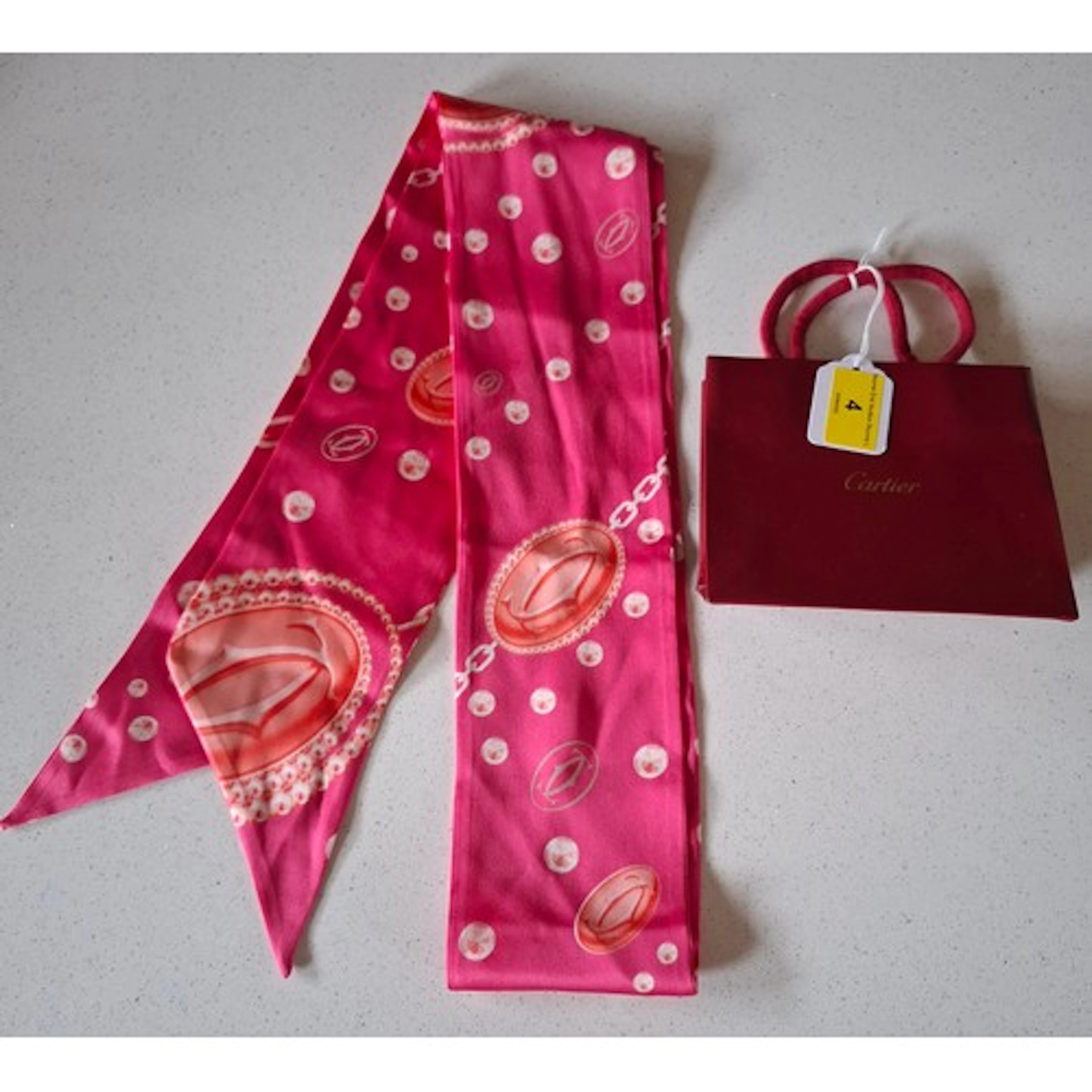 Cartier- A hot pink silk slimline scarf having a gem, jewell...