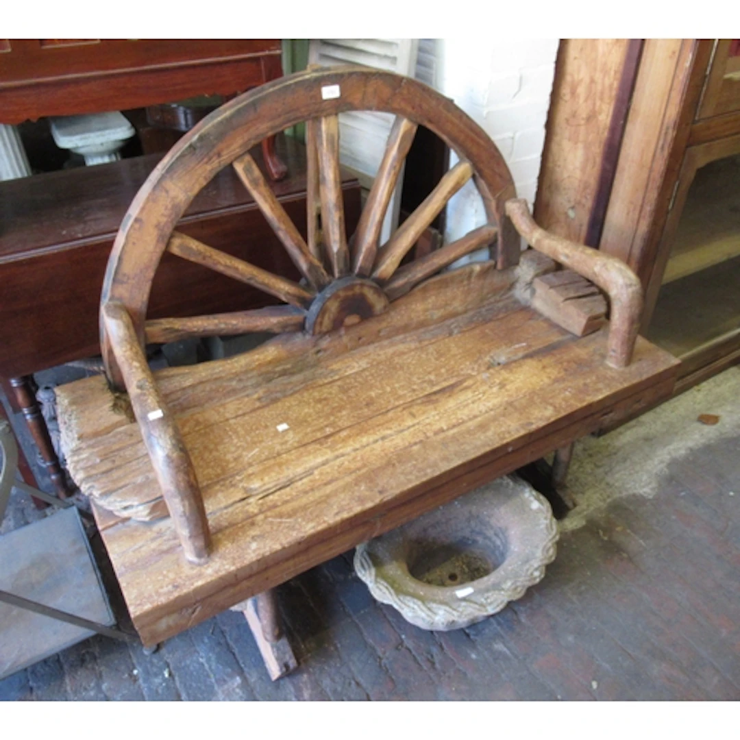 Spanish hardwood wagon wheel bench with open arms above a pl...