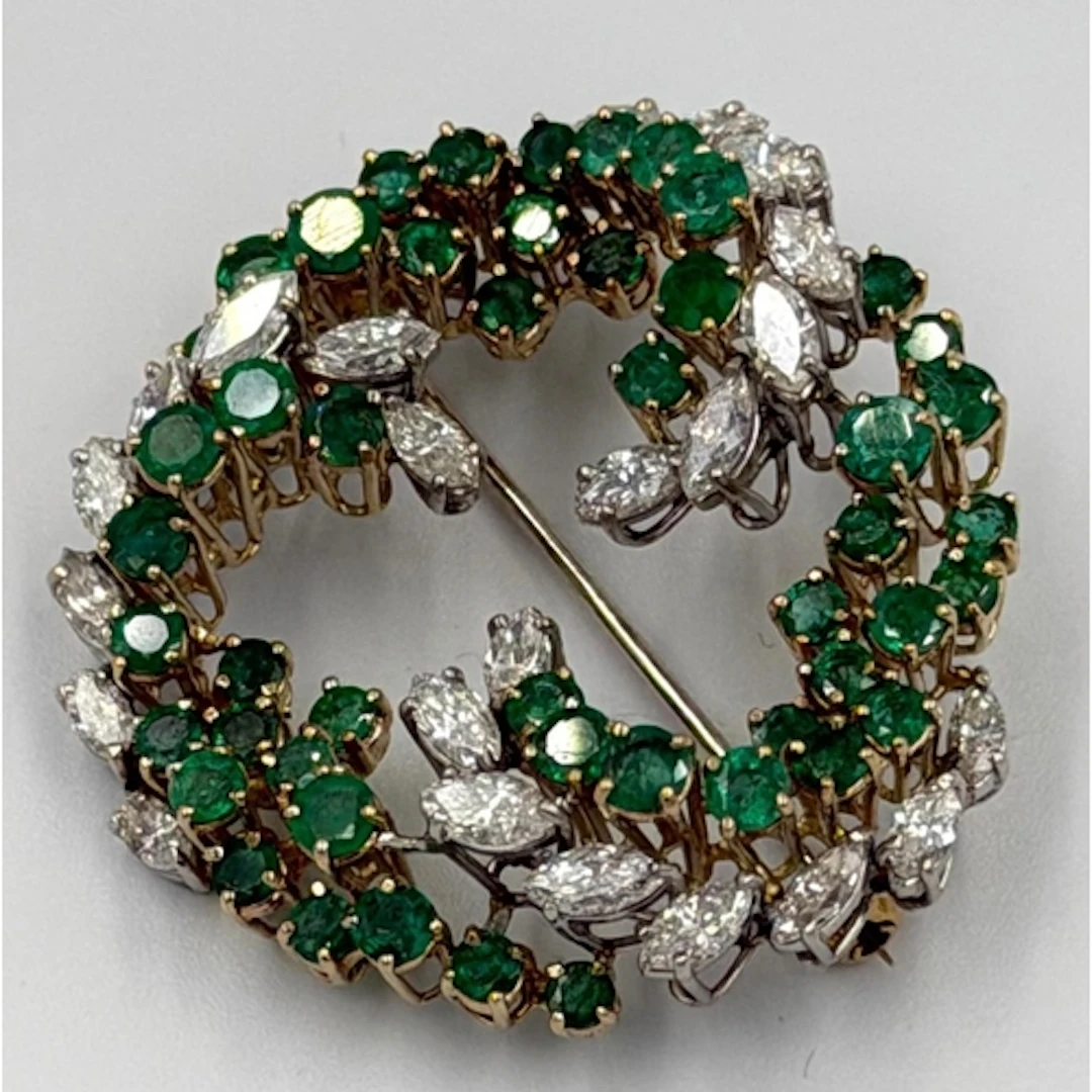 A diamond and emerald swirl brooch, approximate diameter 42m...