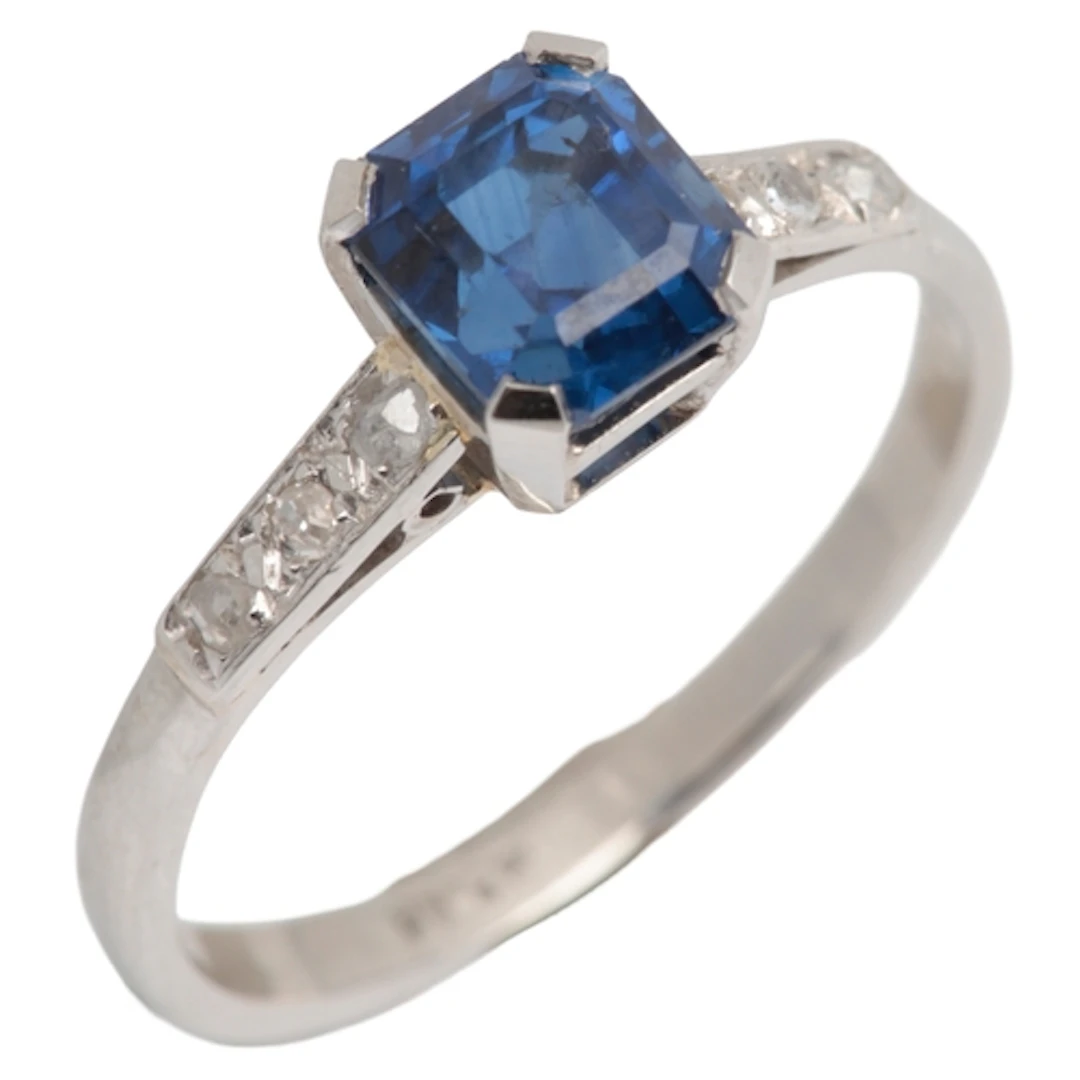 A sapphire and diamond ring, claw-set with a step-cut sapphi...