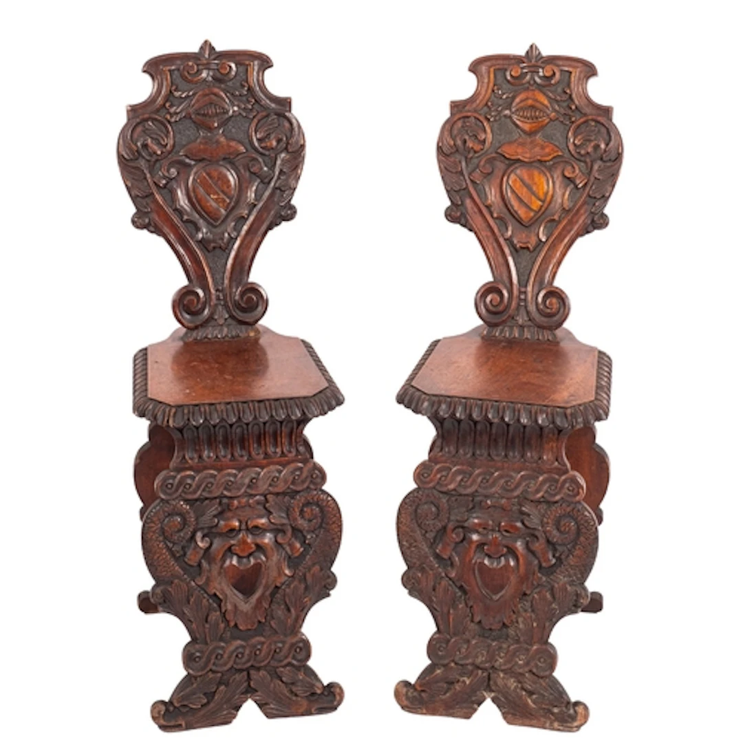 A pair of Italian carved walnut hall chairs, in 17th century...