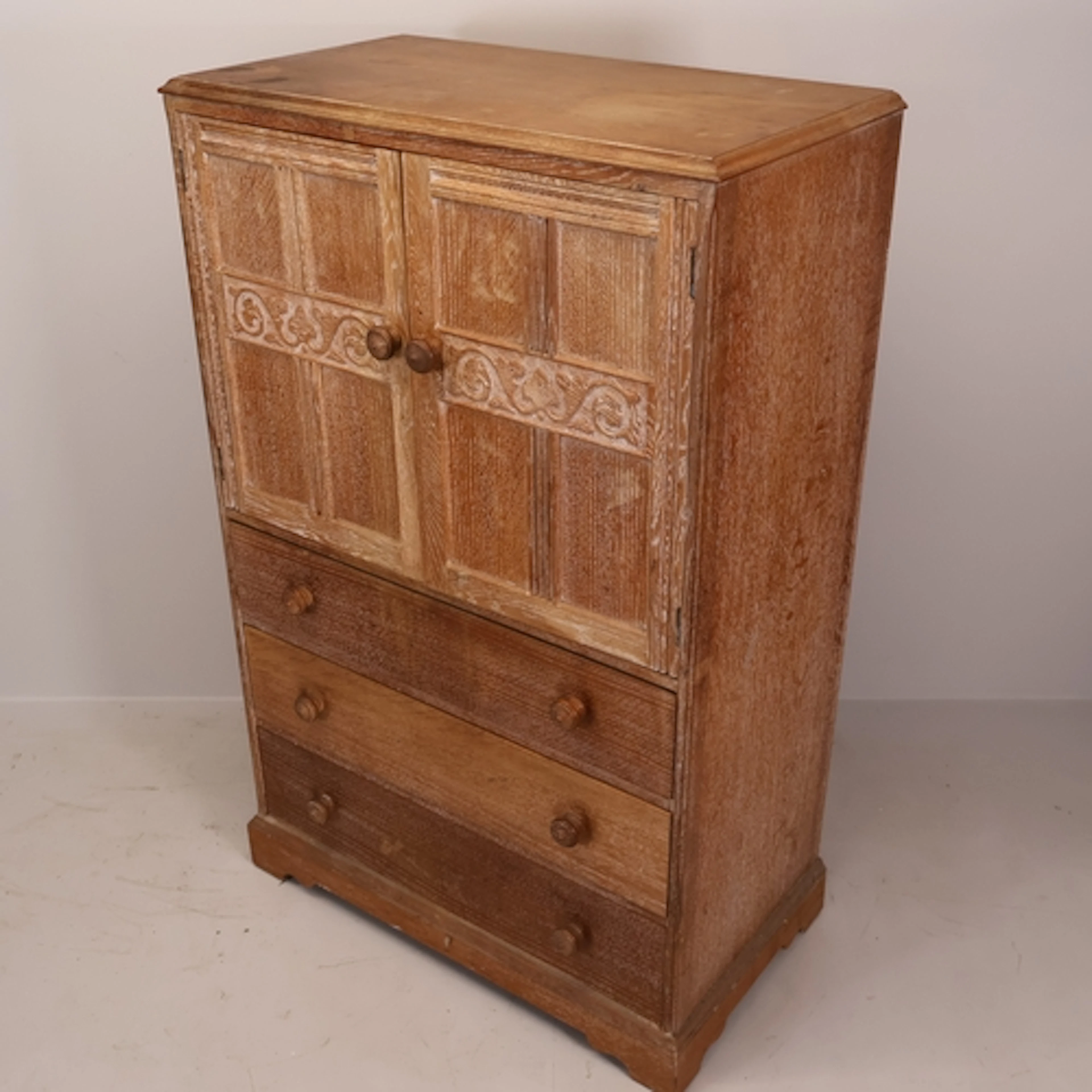 A vintage limed oak tallboy cabinet over three long drawers,...