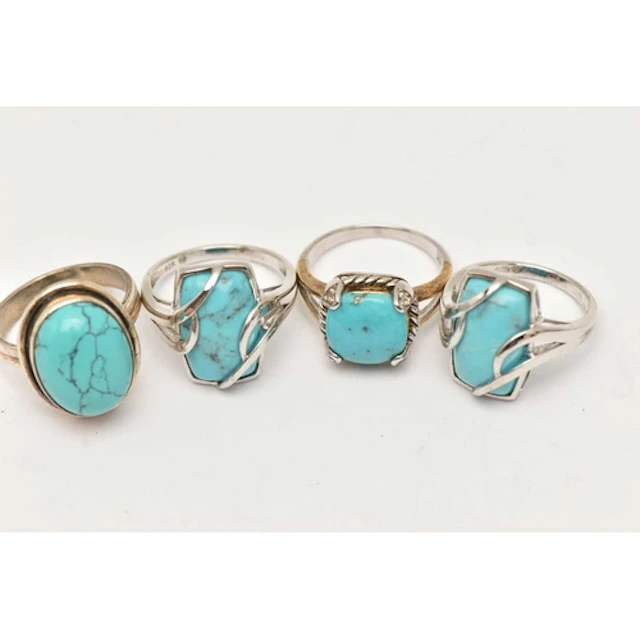 FOUR WHITE METAL TURQUOISE/DYED HOWLITE RINGS, each of a dif...