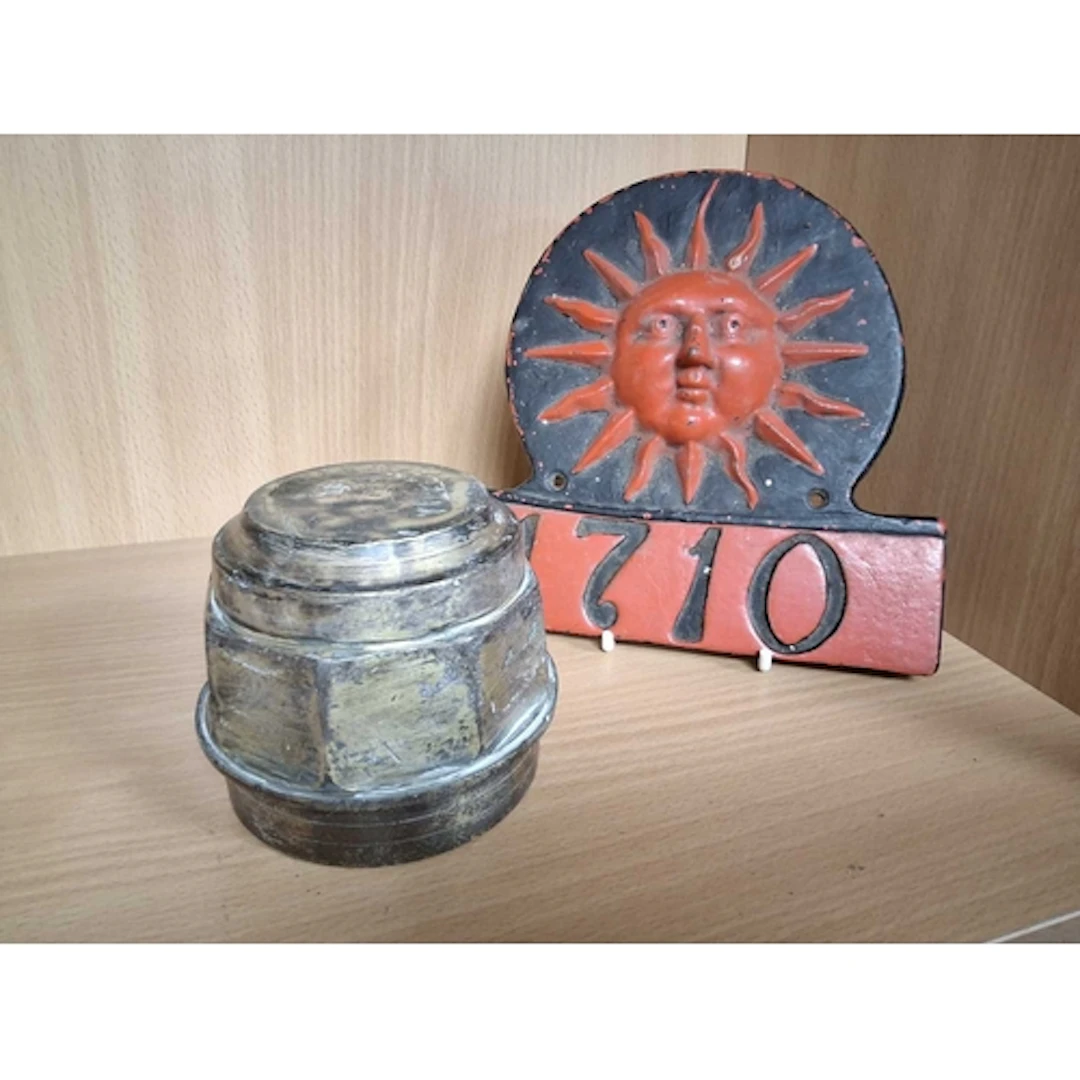 A FIRE INSURANCE PLAQUE AND A BRASS WHEEL NUT, the painted S...