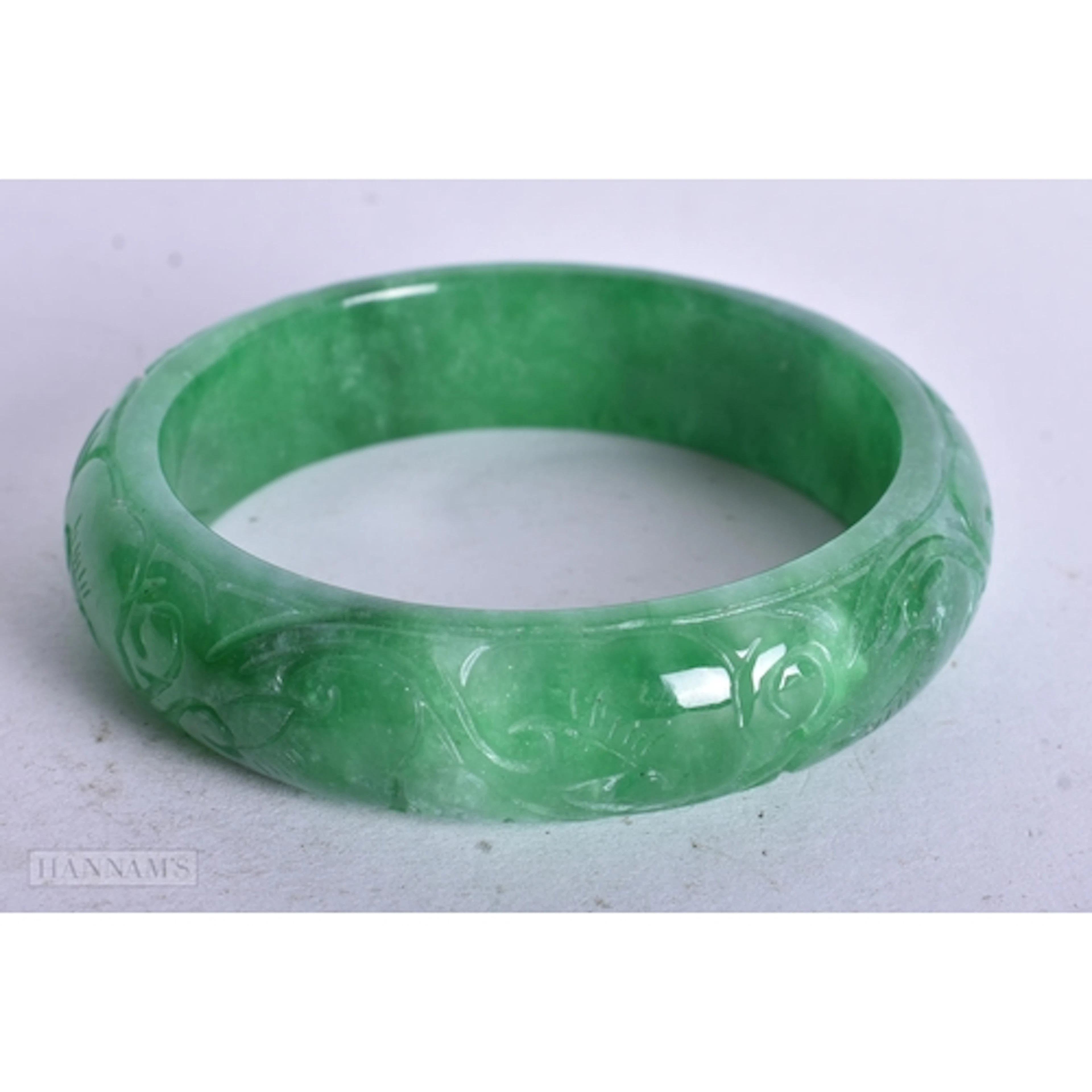A CARVED GREEN JADE BANGLE. 5.3 internal diameter