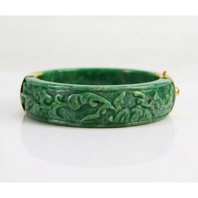A Chinese carved jade hinged bangle in 14K yellow gold mount...
