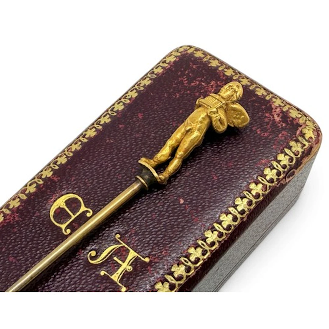 A stick pin mounted with a yellow gold figure of Eros, the f...
