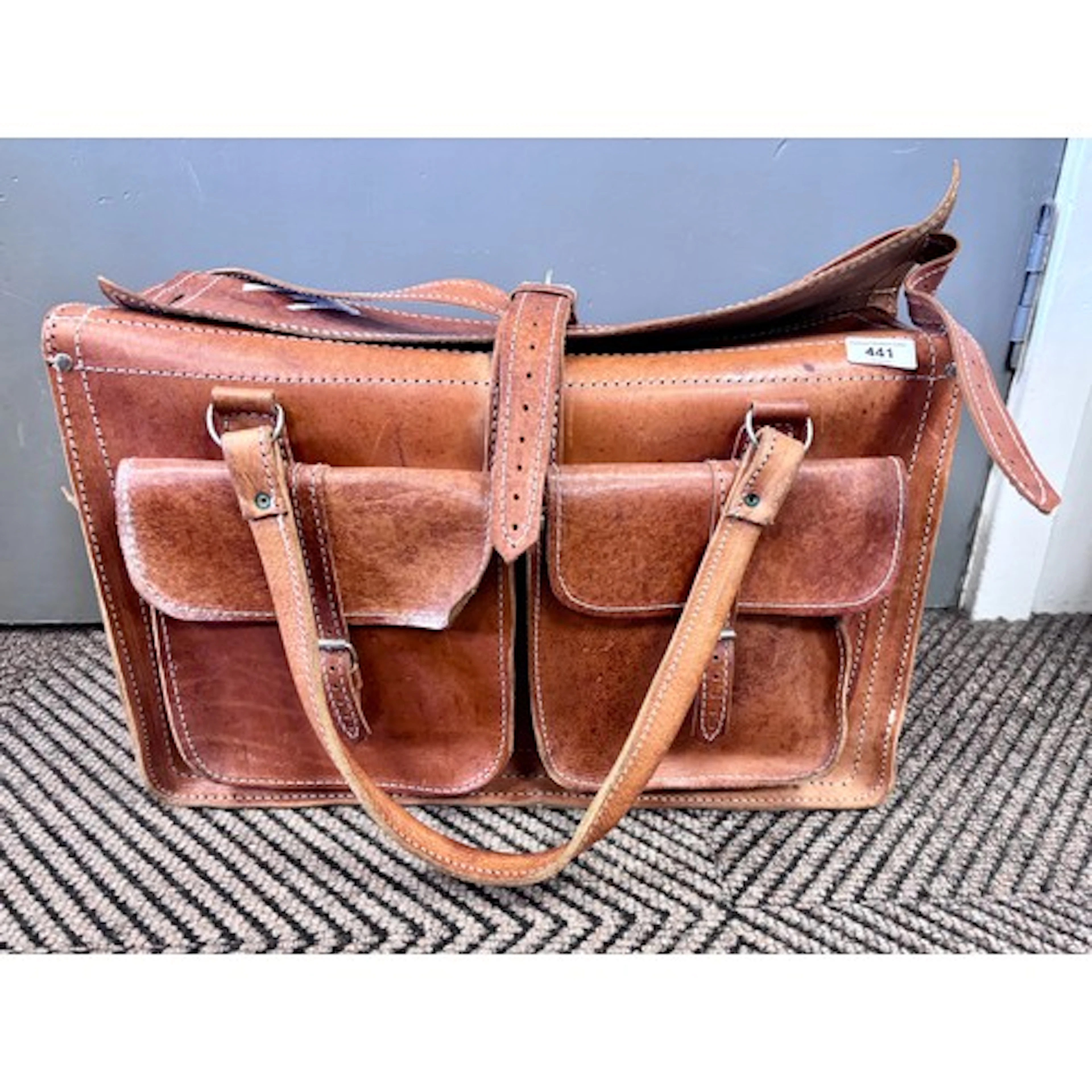 Large tan leather satchel with two front pockets.