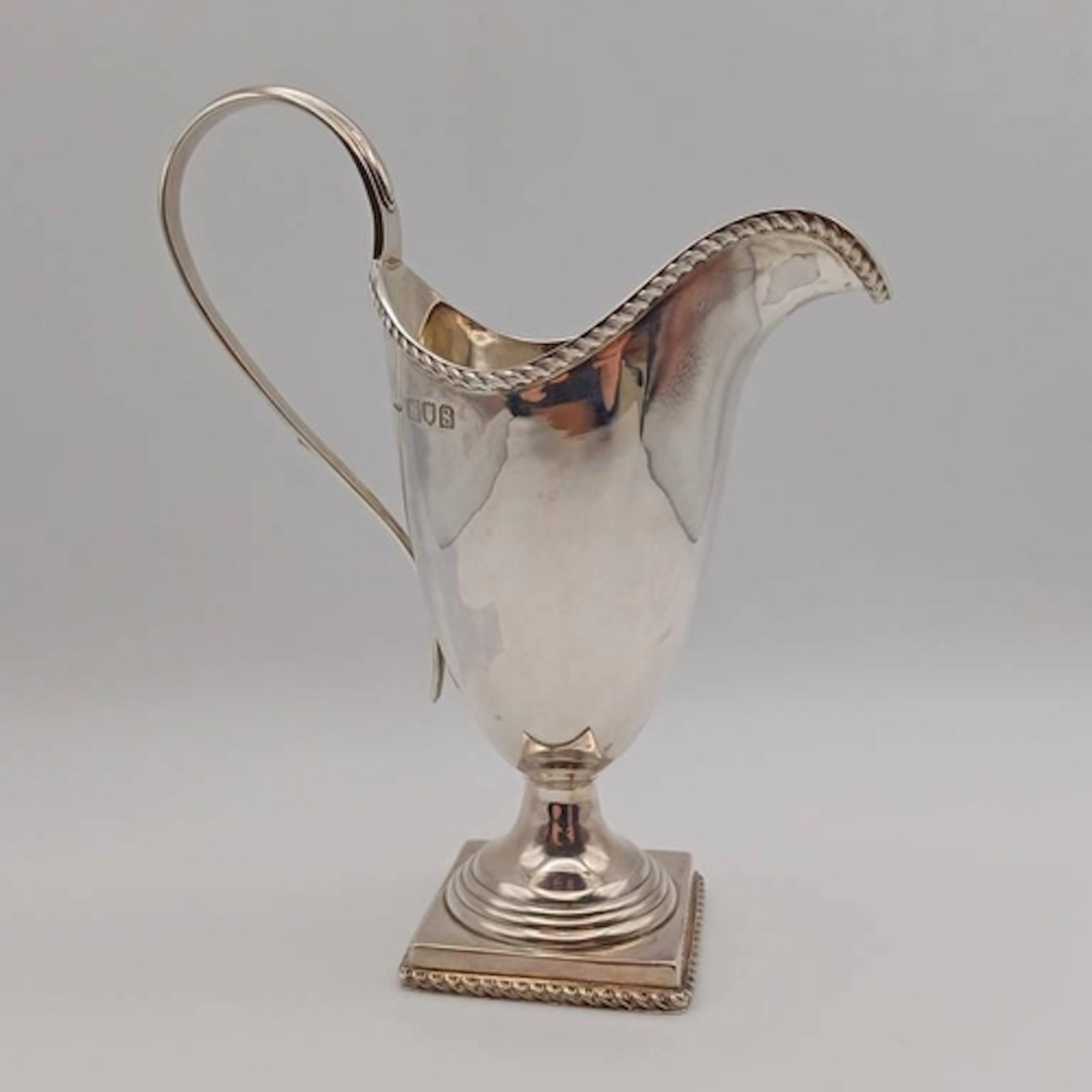 A SILVER CREAM JUG ON SQUARE BASE WITH ROPEWORK DECORATION B...