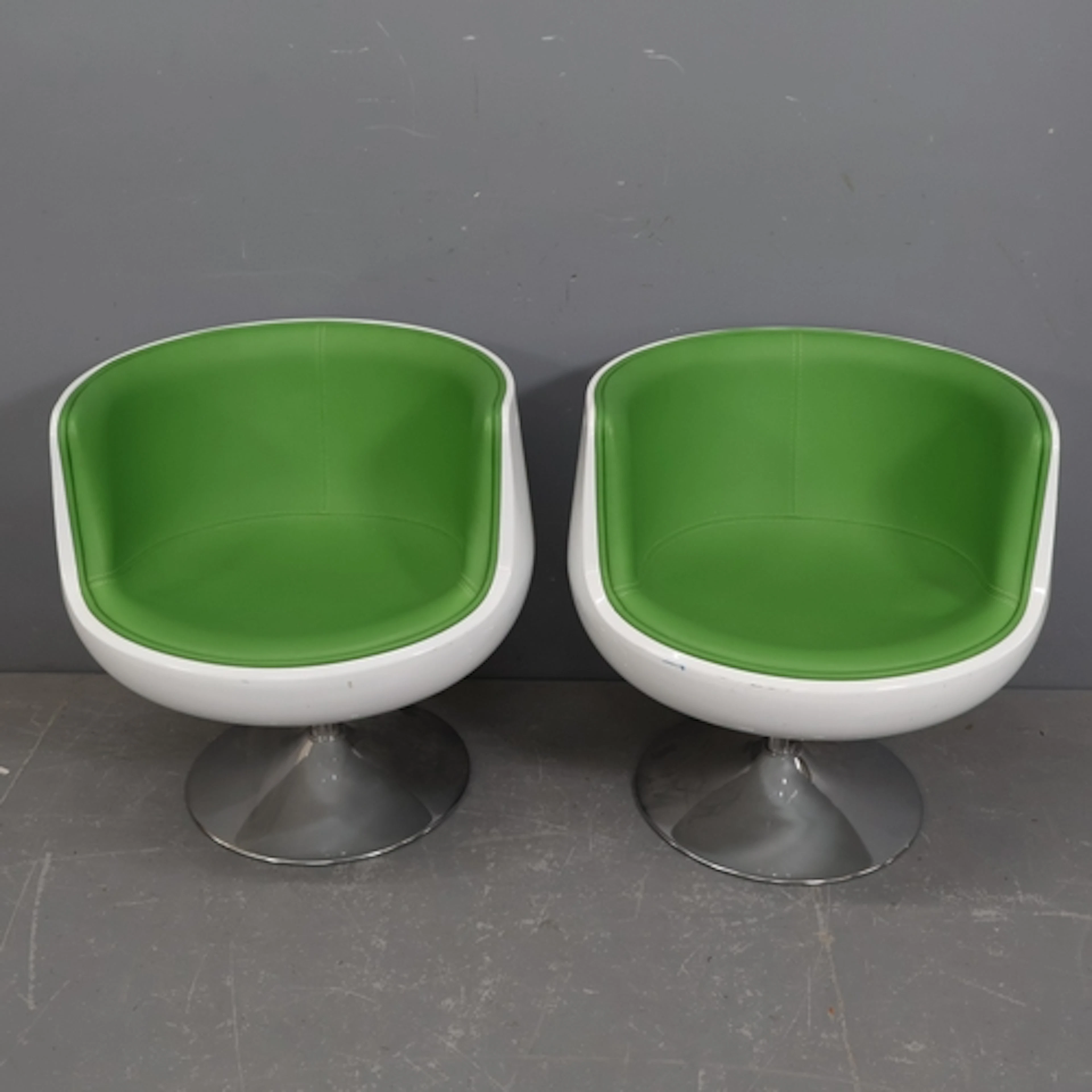 A pair of contemporary swivel cup chairs, the green faux-lea...